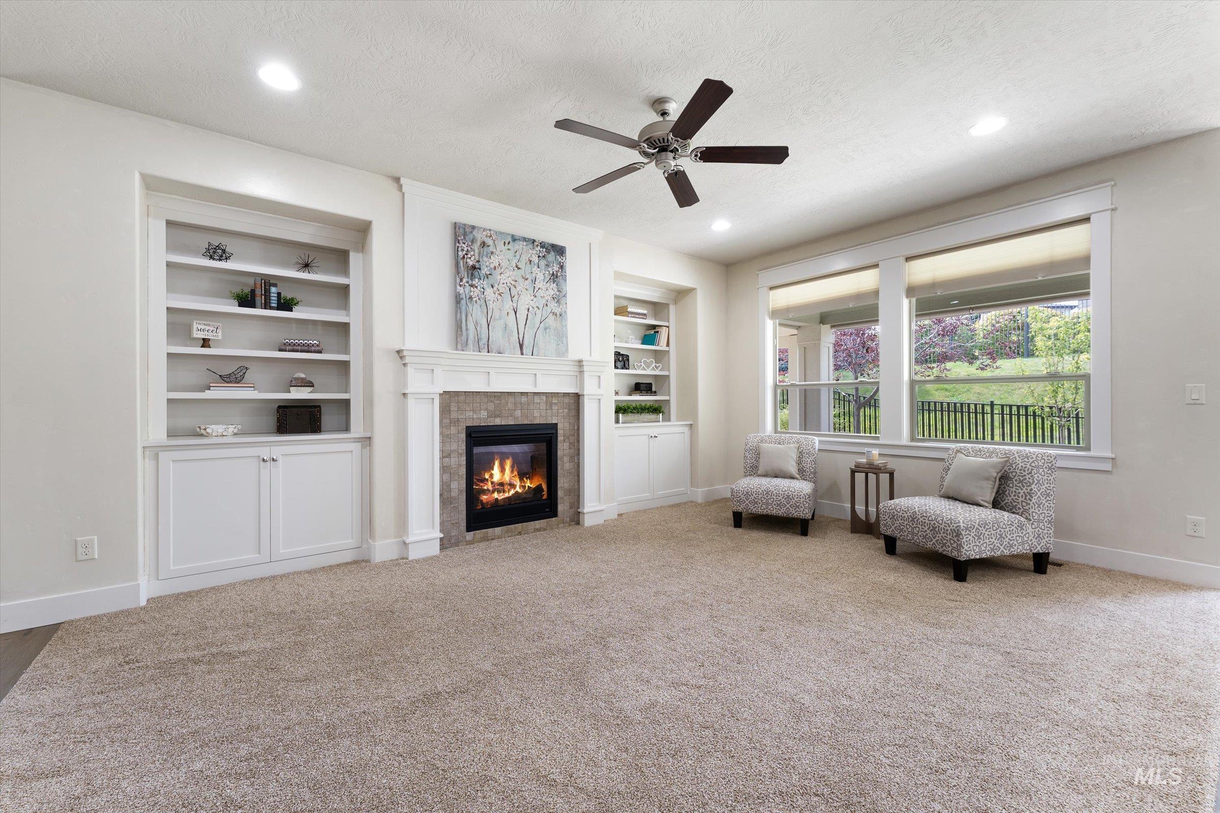 Sitting room featuring a fireplace, a textured ceiling, light colored carpet, built in features, and a ceiling fan