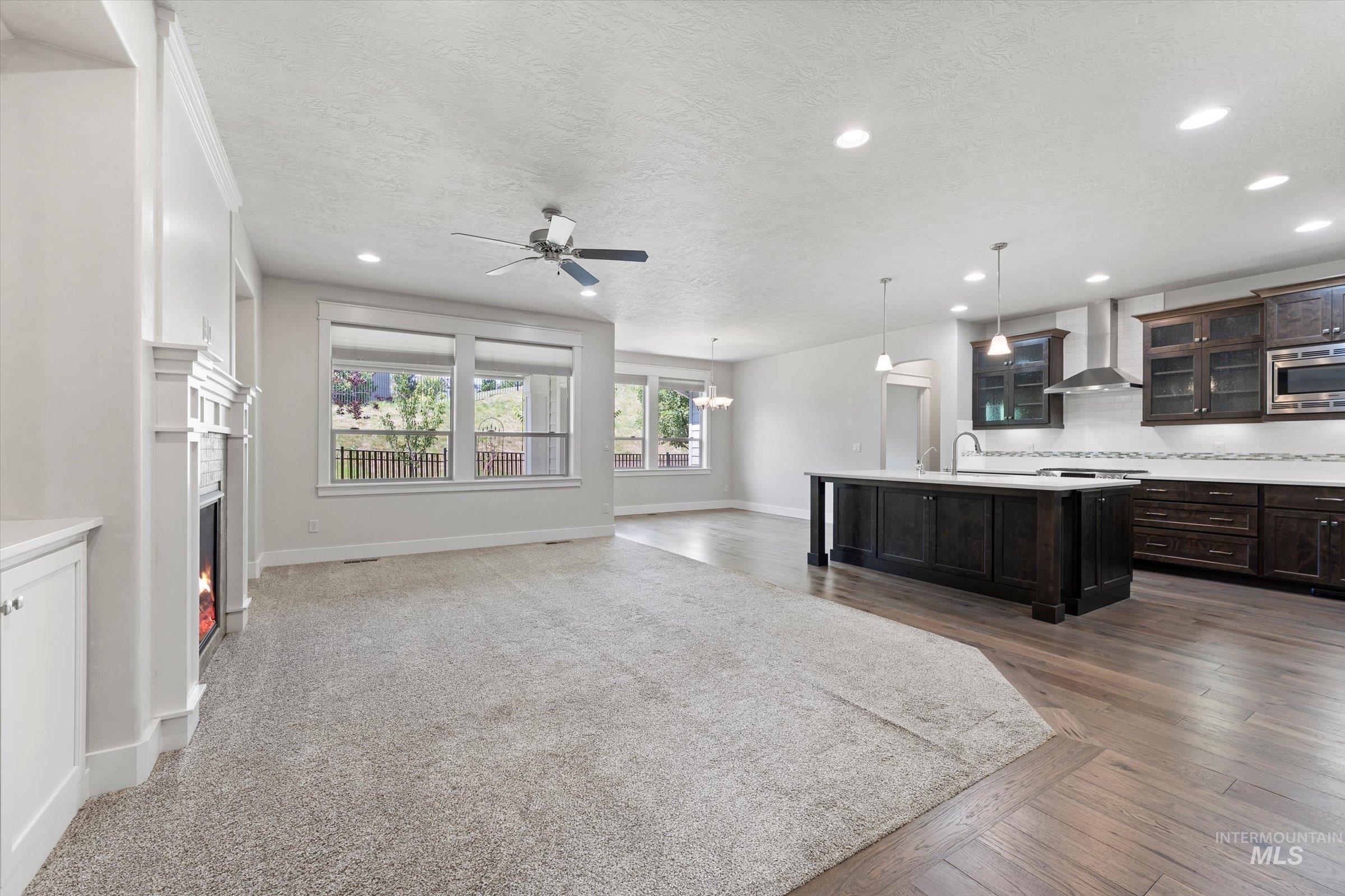Kitchen with wall chimney range hood, stainless steel microwave, ceiling fan, recessed lighting, and open floor plan
