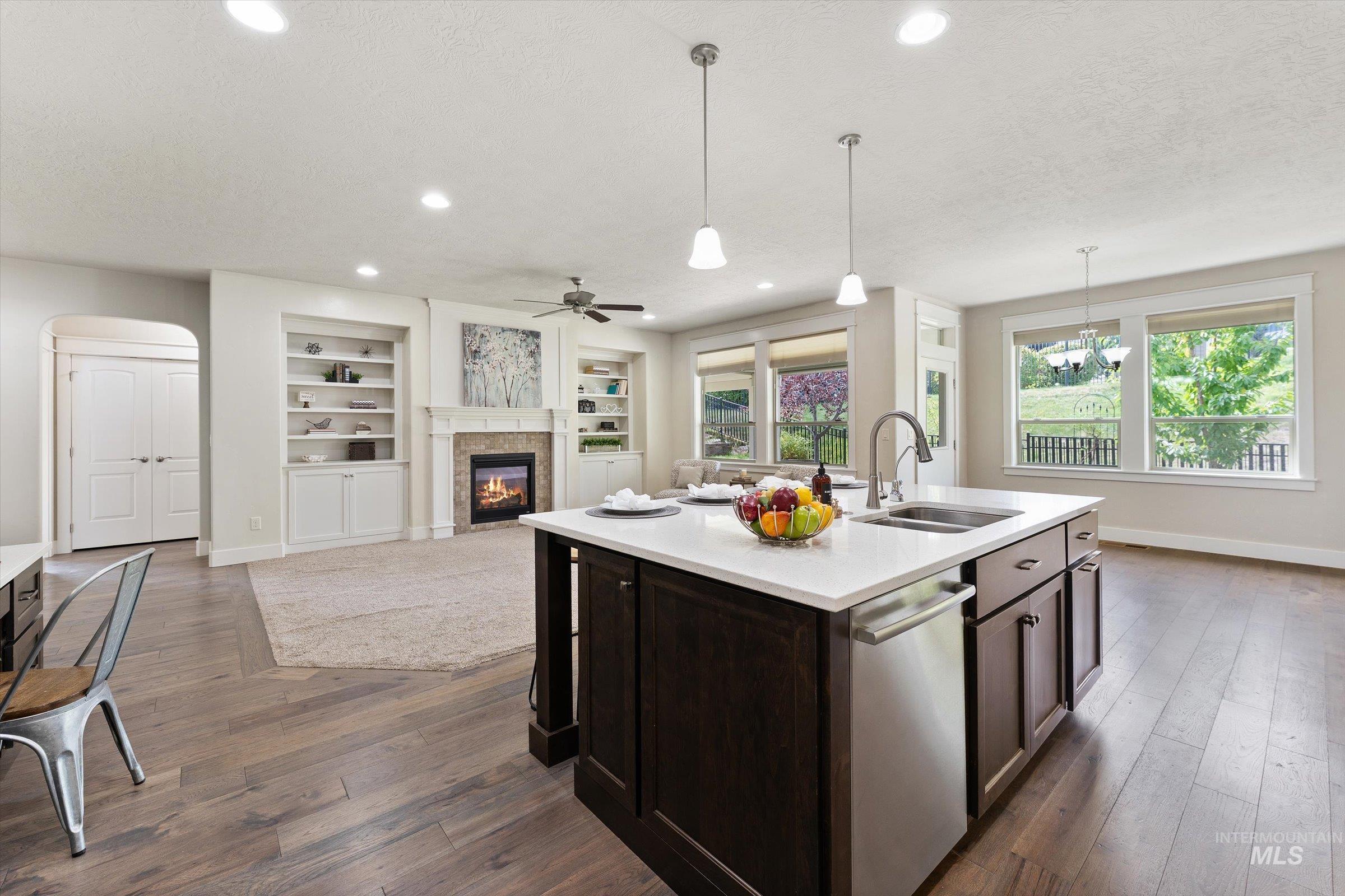 Kitchen featuring built in shelves, pendant lighting, a tile fireplace, stainless steel dishwasher, and dark brown cabinets