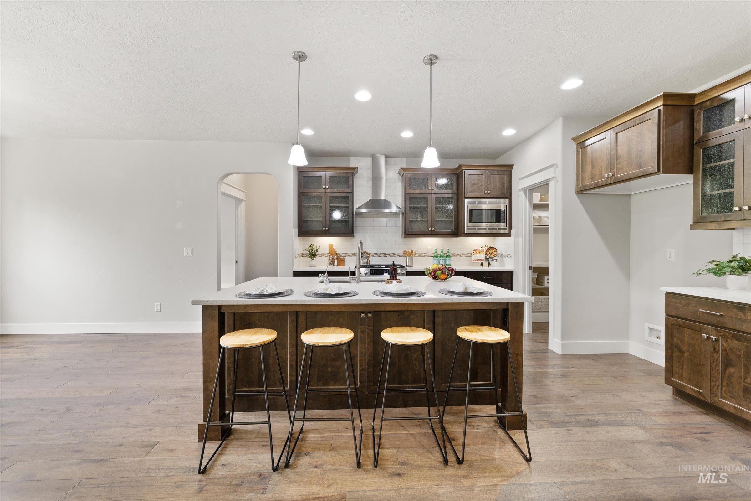 Kitchen with glass insert cabinets, arched walkways, a kitchen bar, a kitchen island with sink, and dark brown cabinetry