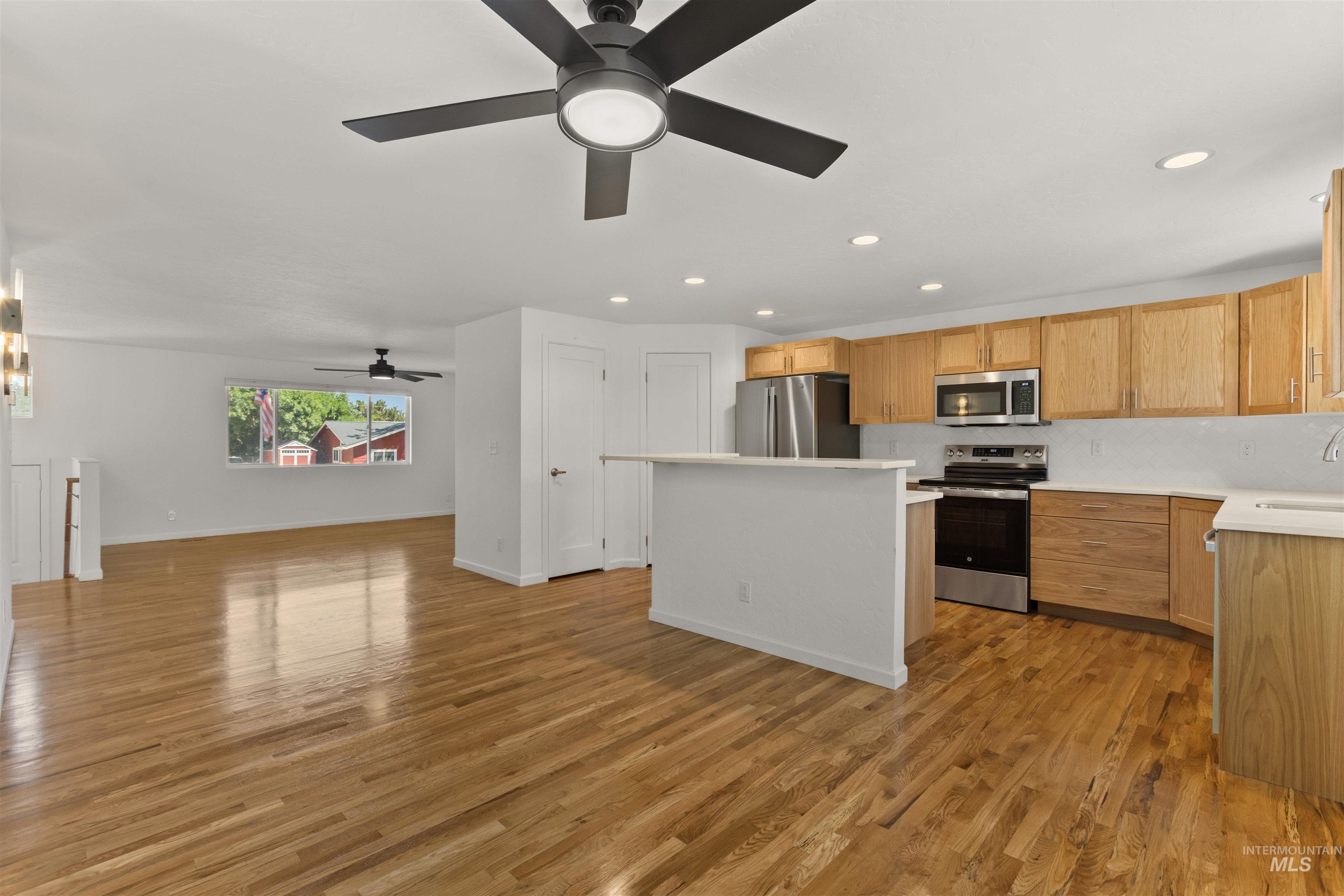 Kitchen featuring appliances with stainless steel finishes, a kitchen island, open floor plan, light countertops, and a ceiling fan