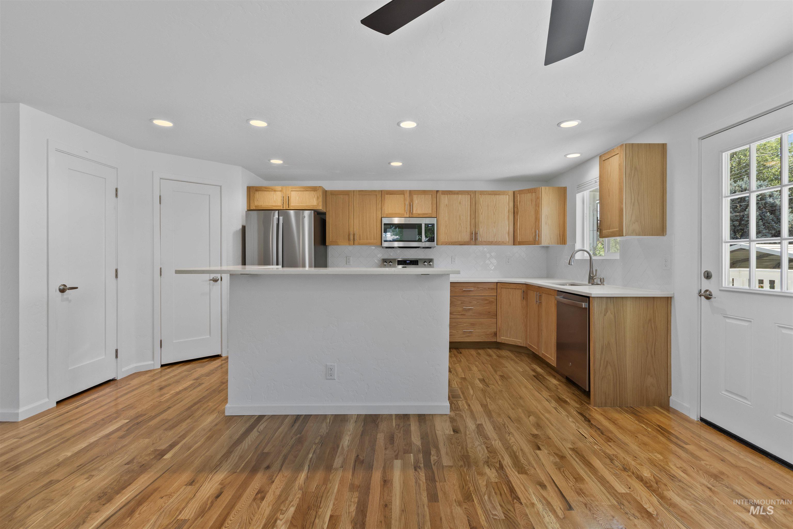Kitchen featuring stainless steel appliances, a ceiling fan, light countertops, light wood finished floors, and recessed lighting