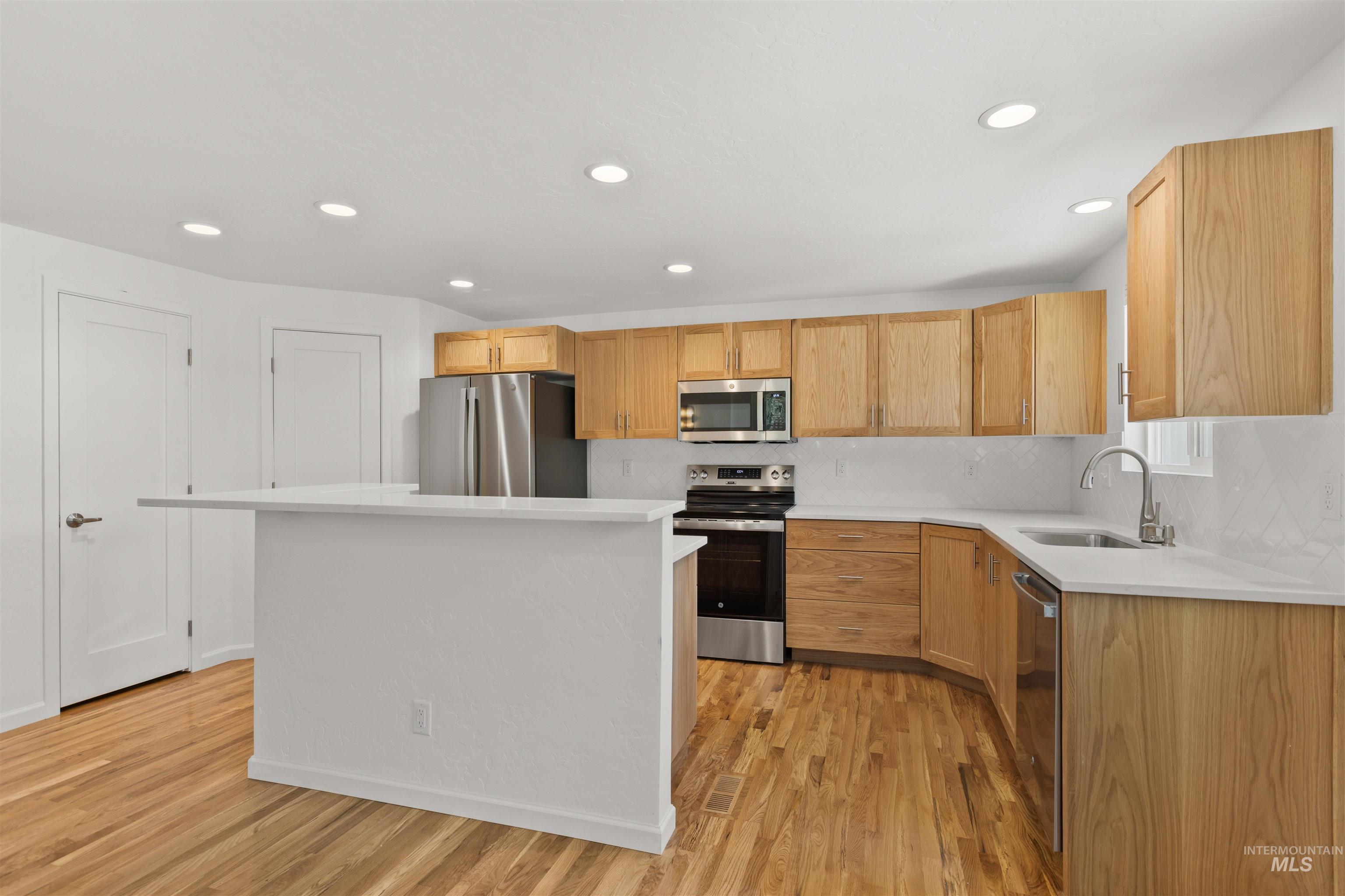 Kitchen featuring appliances with stainless steel finishes, light wood-style flooring, light countertops, a kitchen island, and recessed lighting