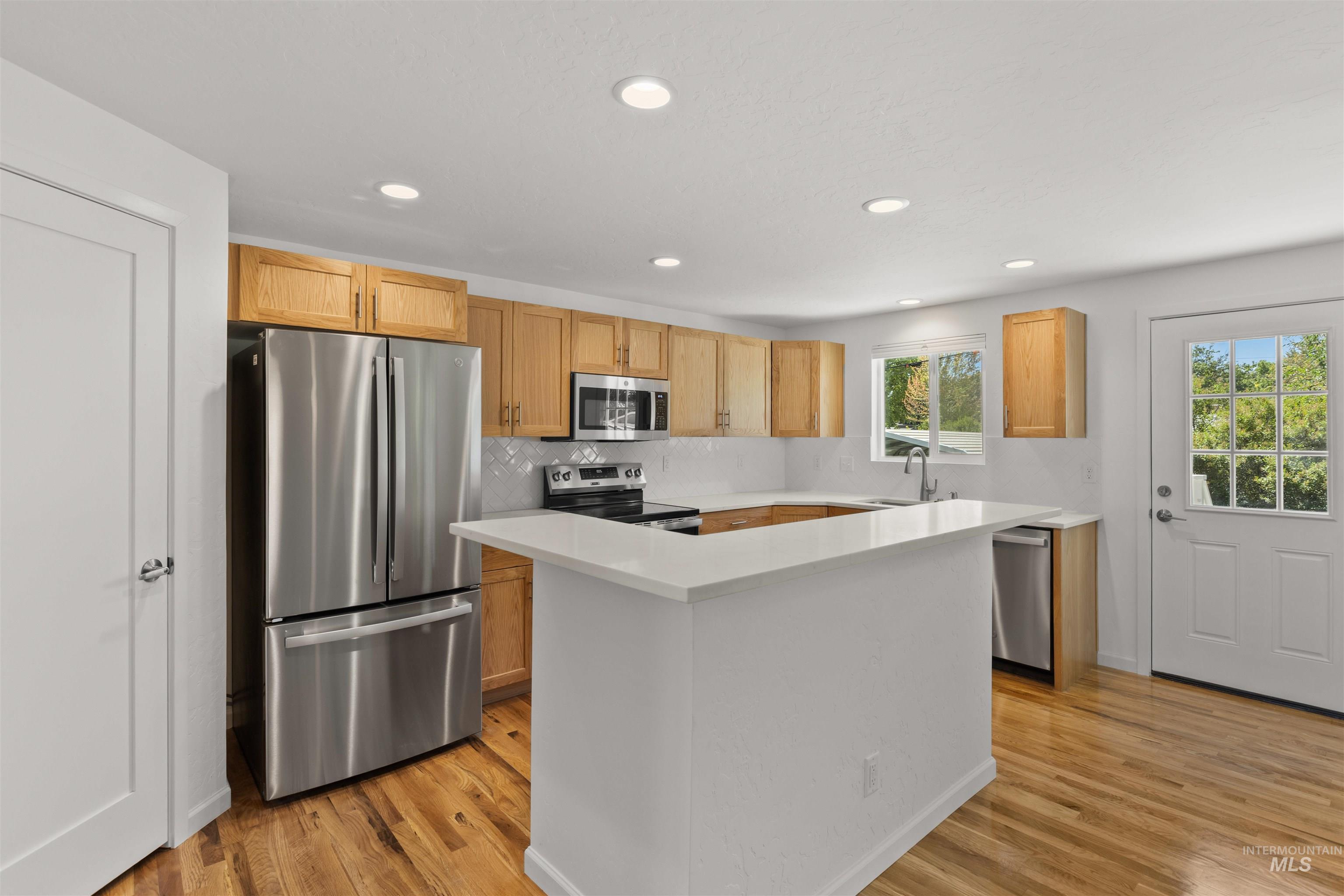 Kitchen with stainless steel appliances, light wood finished floors, light countertops, a kitchen island, and recessed lighting