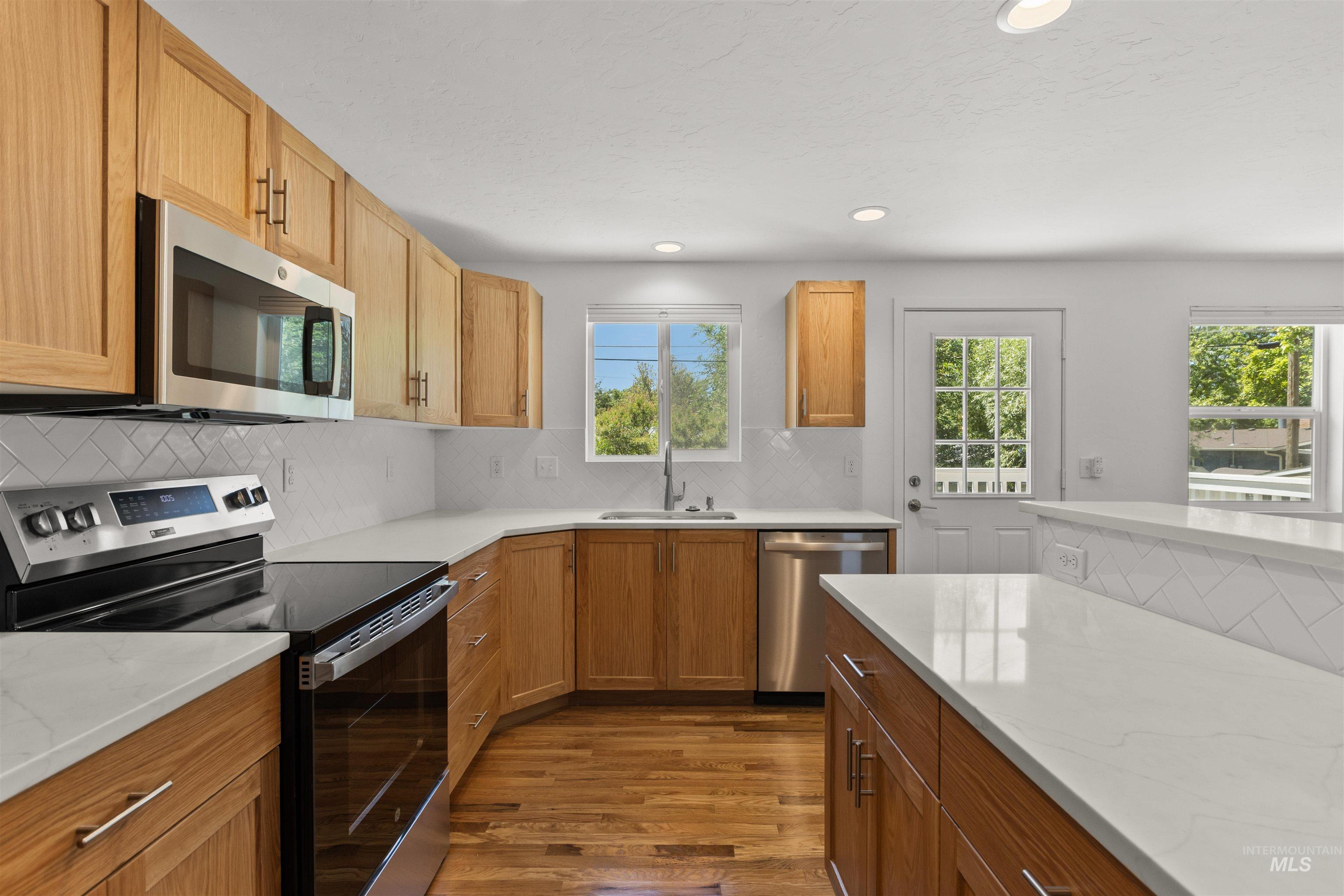 Kitchen featuring appliances with stainless steel finishes, plenty of natural light, dark wood-style flooring, decorative backsplash, and recessed lighting