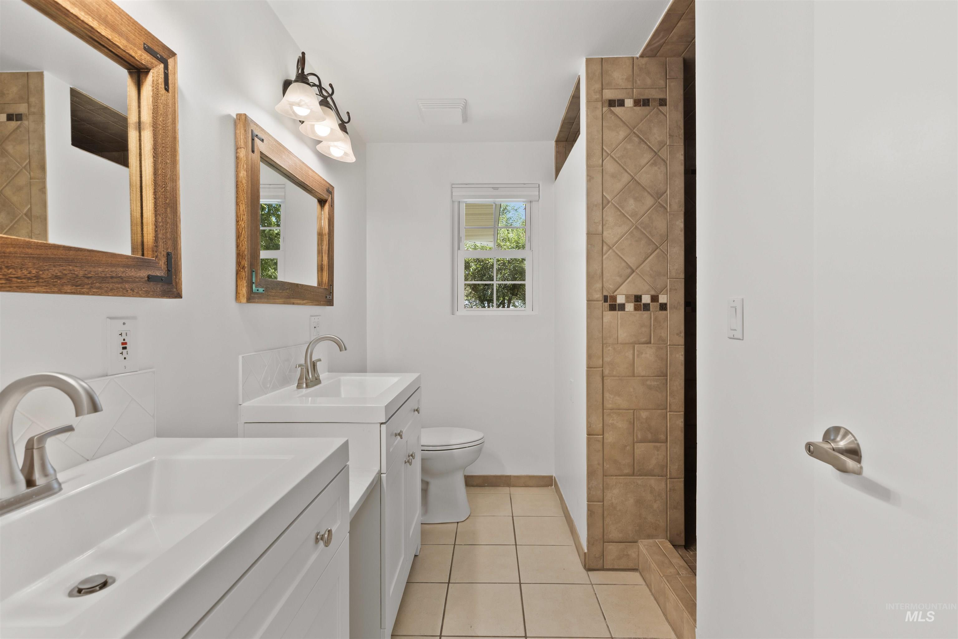 Full bathroom featuring two vanities, tile patterned flooring, and tiled shower