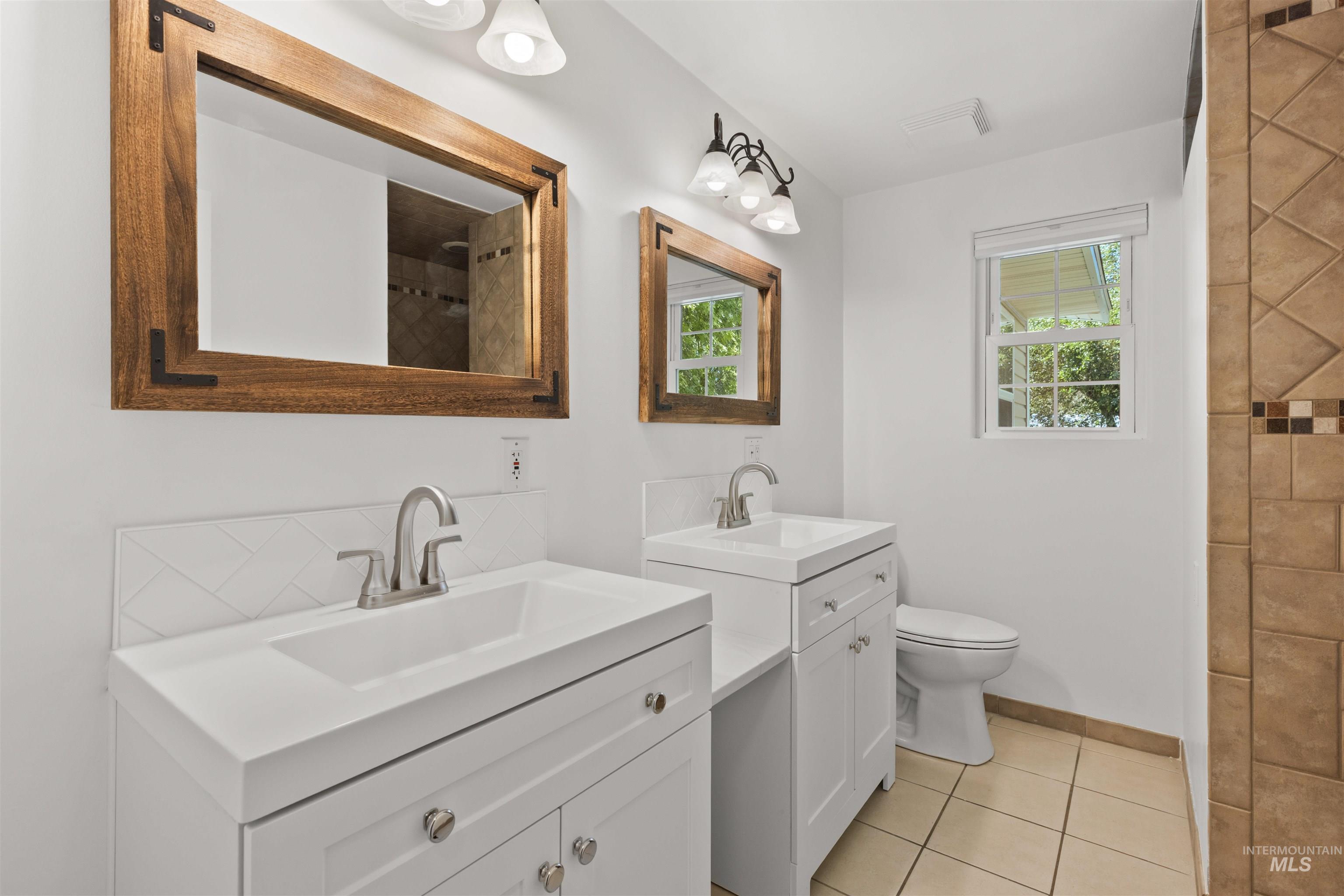 Full bathroom with two vanities, tile patterned floors, and tiled shower