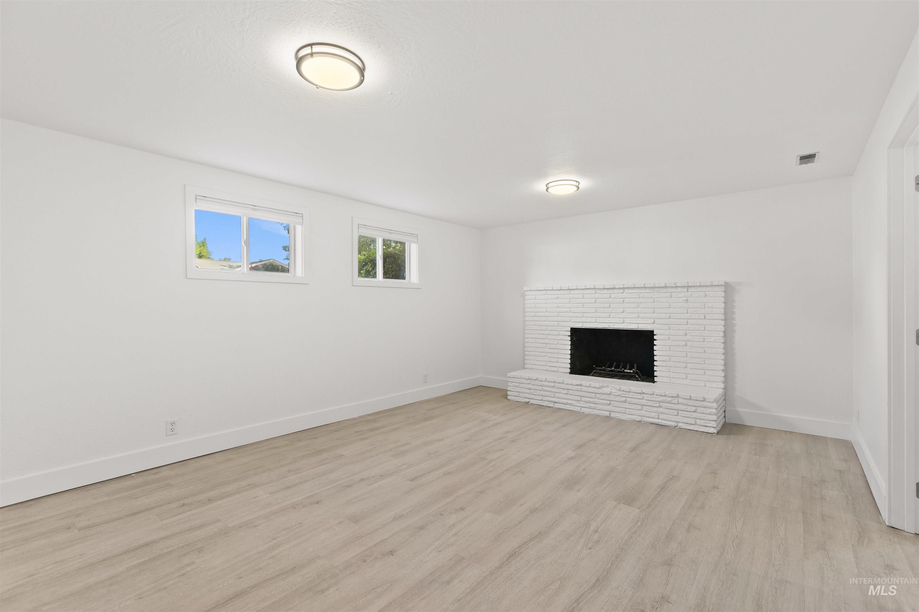 Unfurnished living room featuring light wood finished floors and a brick fireplace