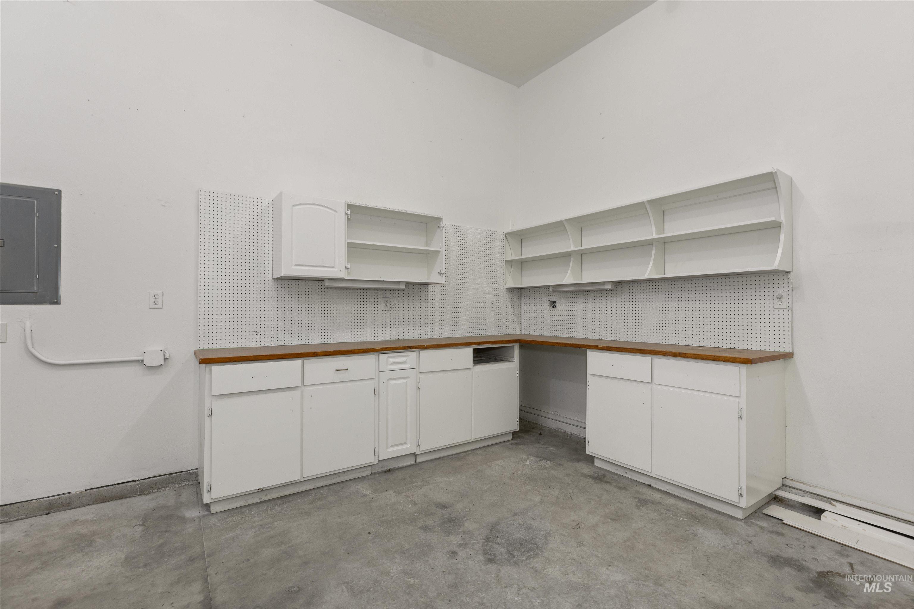 Kitchen featuring electric panel, open shelves, concrete floors, and white cabinets