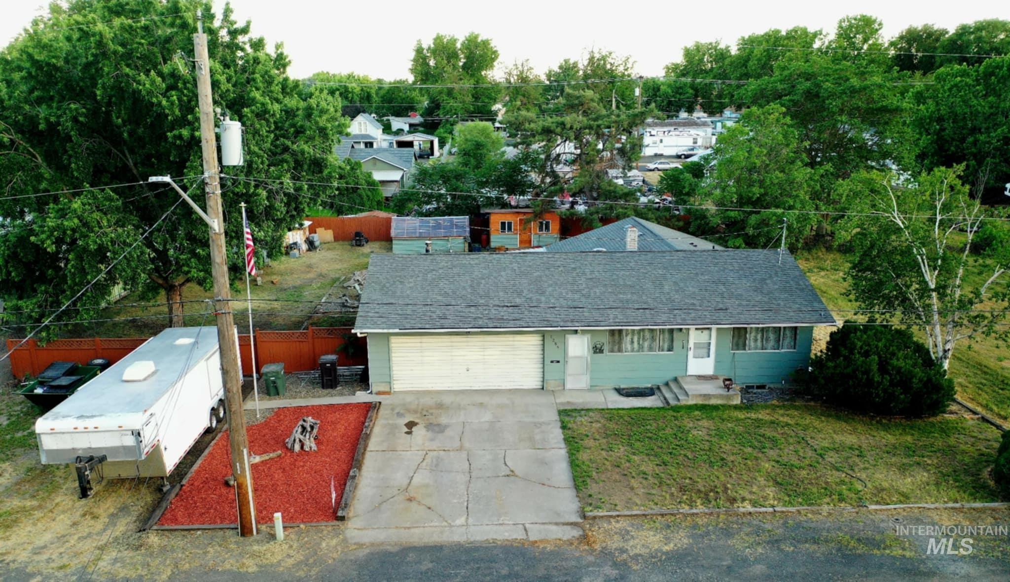 View of front of property with an attached garage, driveway, view of scattered trees, and a shingled roof