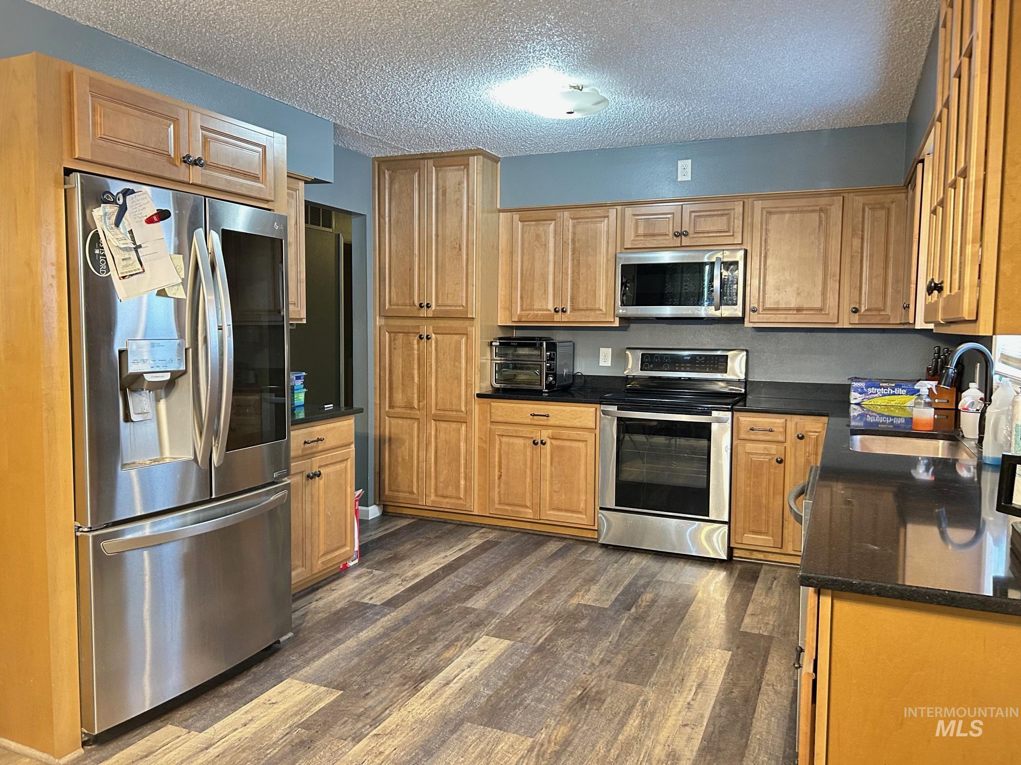 Kitchen featuring appliances with stainless steel finishes, dark countertops, dark wood finished floors, and a textured ceiling