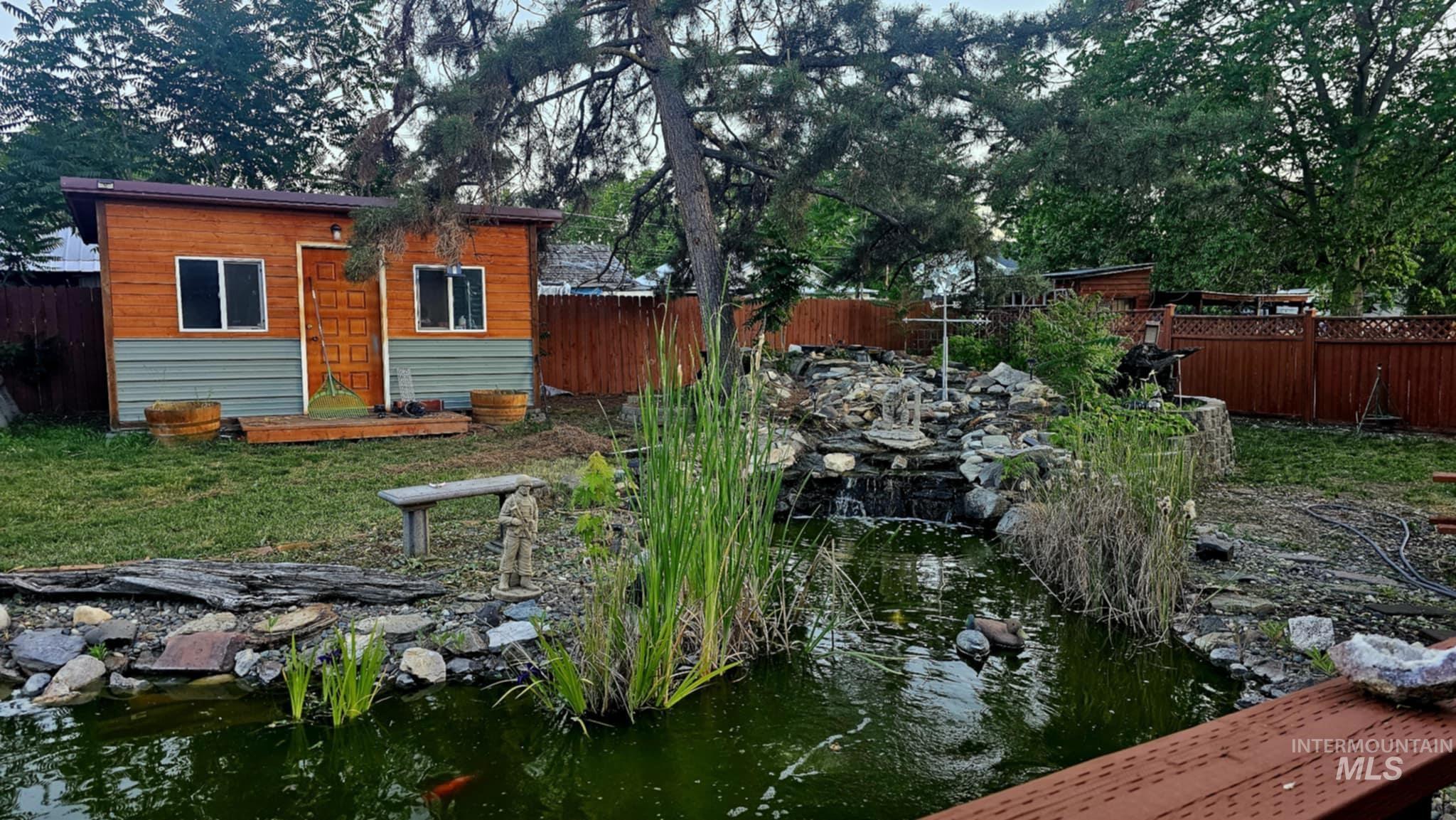 Fenced backyard featuring an outbuilding and a small pond