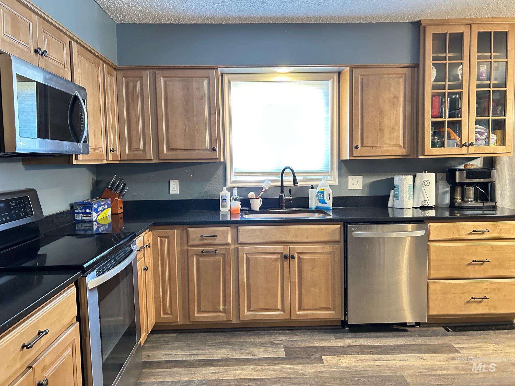 Kitchen with appliances with stainless steel finishes, dark countertops, wood finished floors, glass insert cabinets, and a textured ceiling