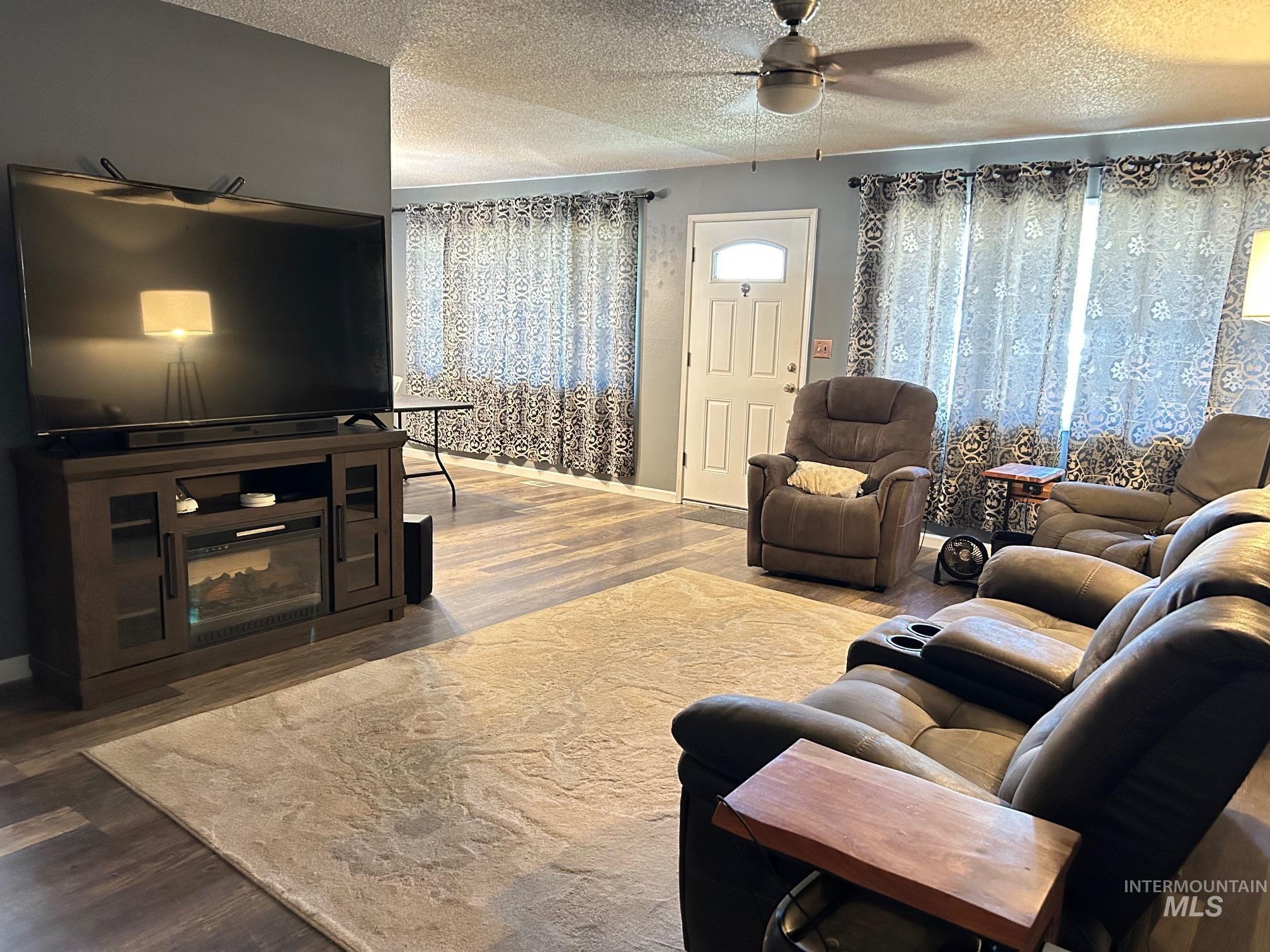 Living area featuring wood finished floors, a textured ceiling, and ceiling fan