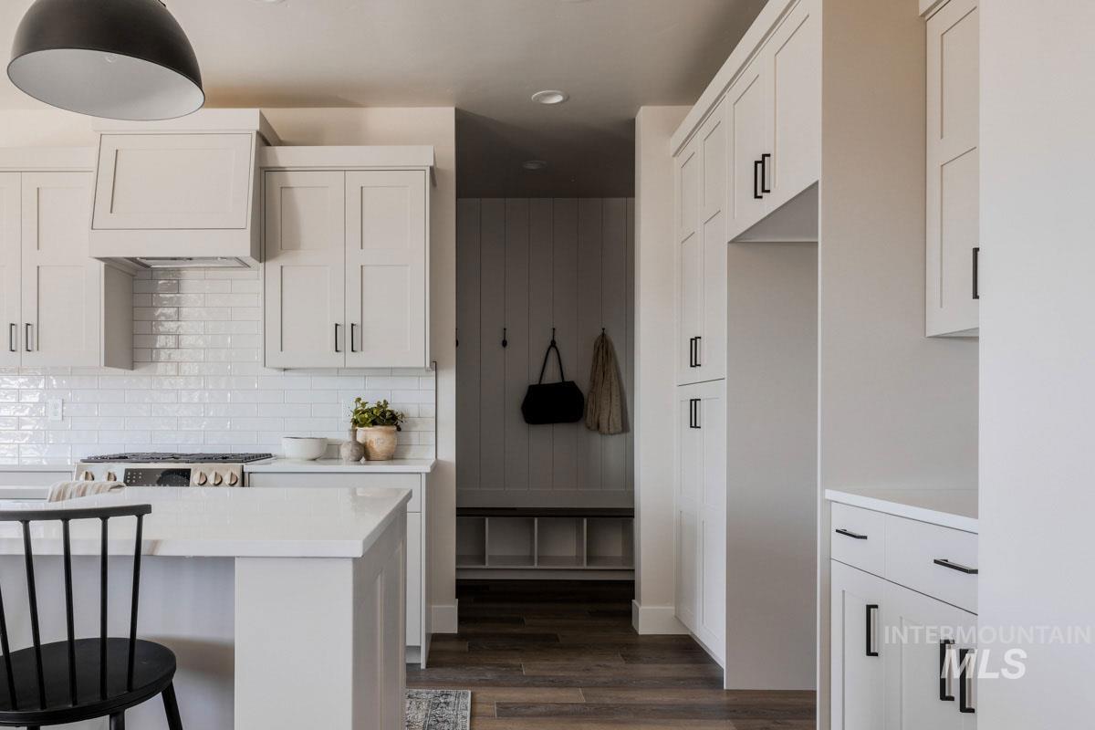 Kitchen with light countertops, dark wood finished floors, custom range hood, a breakfast bar, and backsplash