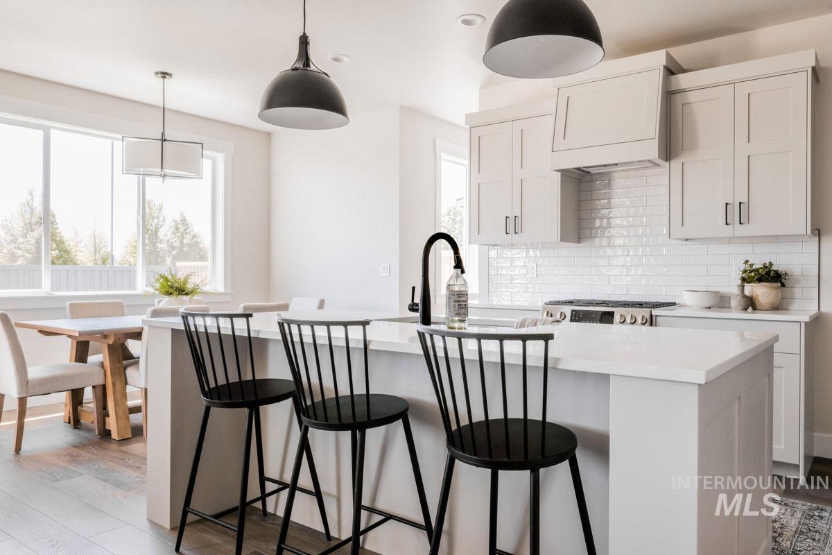 Kitchen with decorative backsplash, light countertops, light wood-type flooring, a center island with sink, and a kitchen breakfast bar