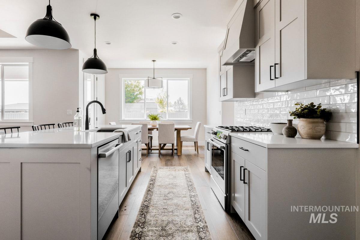Kitchen with stainless steel appliances, custom range hood, light countertops, backsplash, and recessed lighting