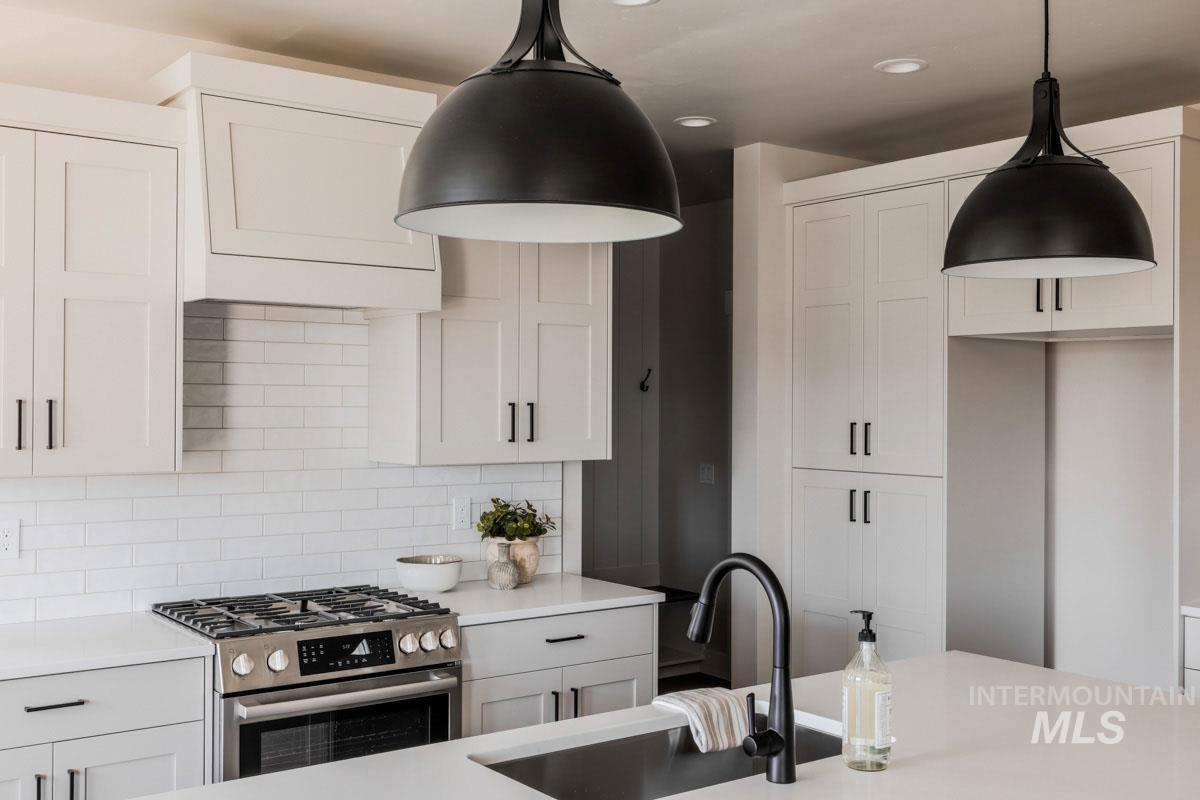 Kitchen featuring stainless steel gas range, light countertops, backsplash, decorative light fixtures, and white cabinets