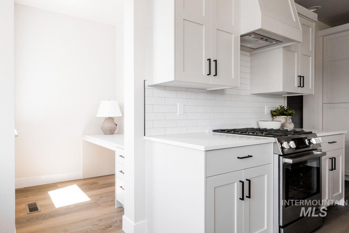 Kitchen featuring stainless steel range with gas stovetop, custom exhaust hood, light countertops, light wood-style floors, and decorative backsplash