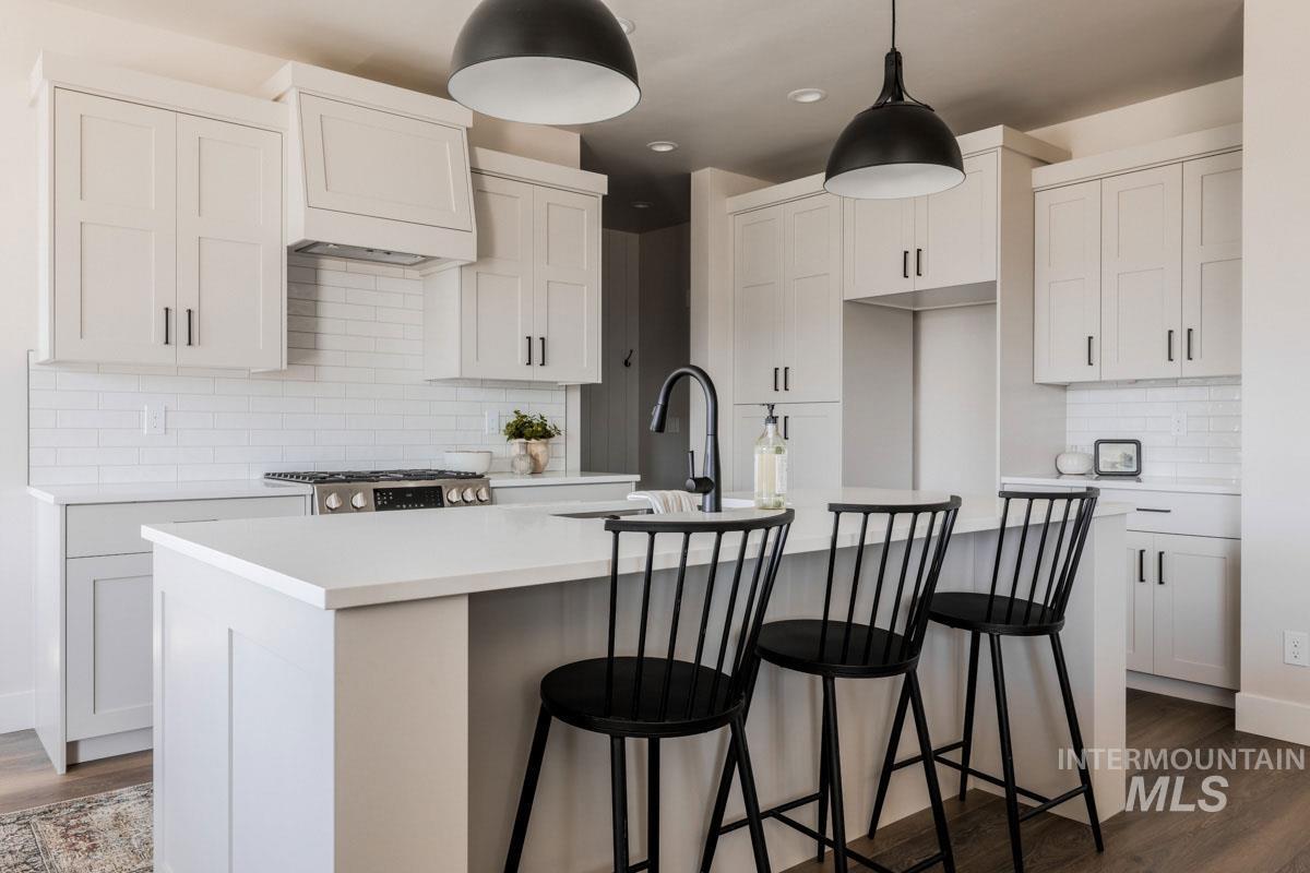 Kitchen with decorative backsplash, dark wood-style floors, a kitchen island with sink, light countertops, and pendant lighting