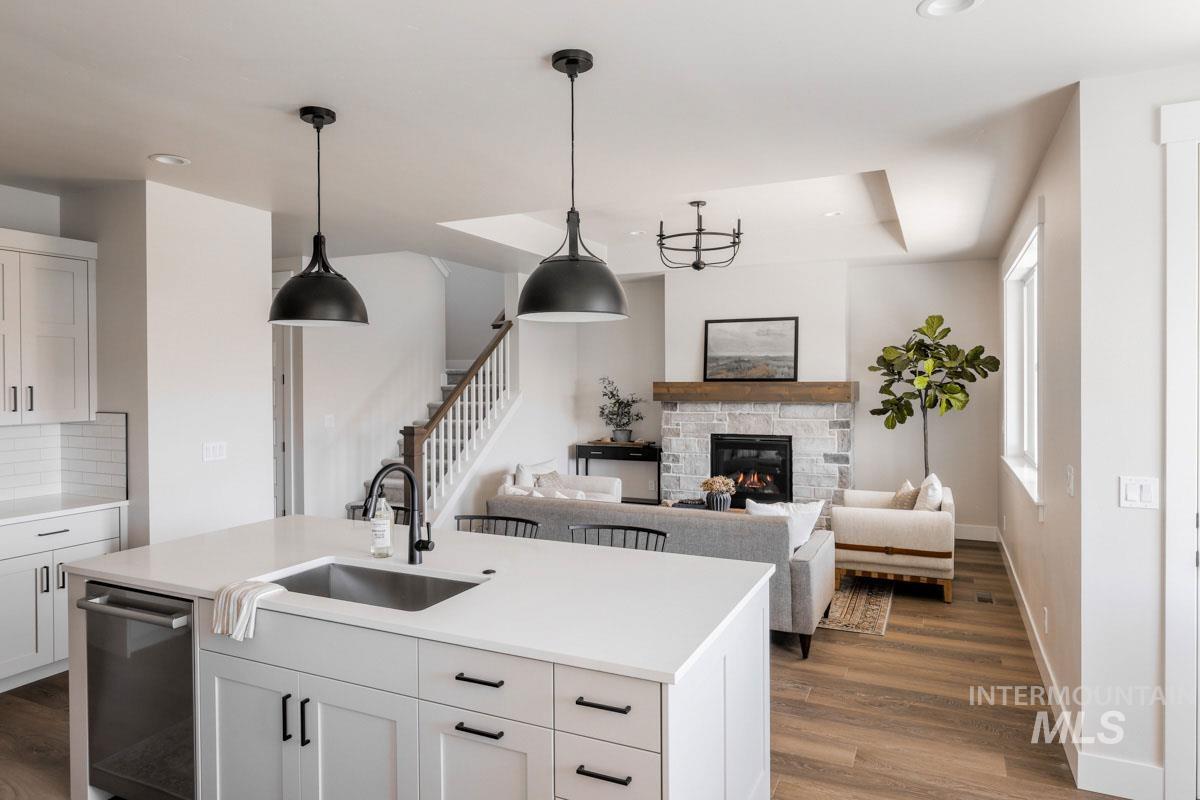 Kitchen featuring wood finished floors, dishwasher, a stone fireplace, light countertops, and a center island with sink