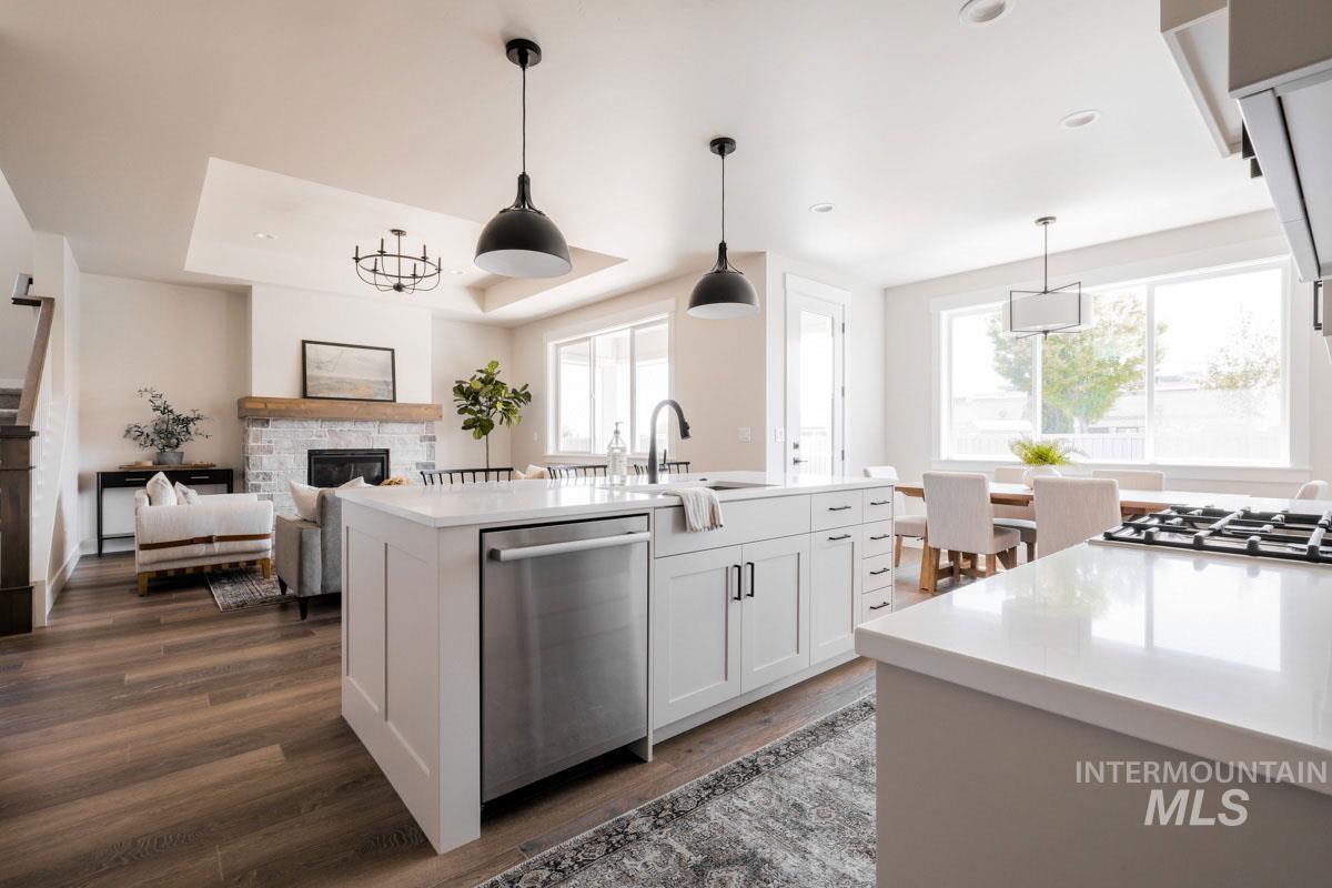 Kitchen with dishwasher, a stone fireplace, dark wood-style floors, light countertops, and a kitchen island with sink