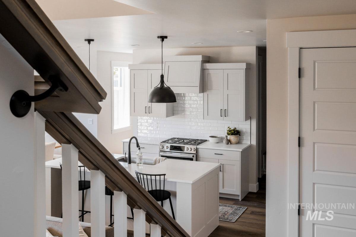Kitchen featuring gas stove, dark wood-style flooring, white cabinets, a kitchen bar, and light countertops