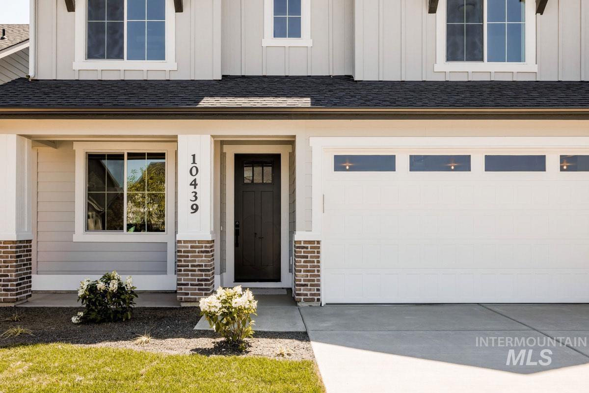 Entrance to property featuring board and batten siding, a garage, brick siding, and driveway