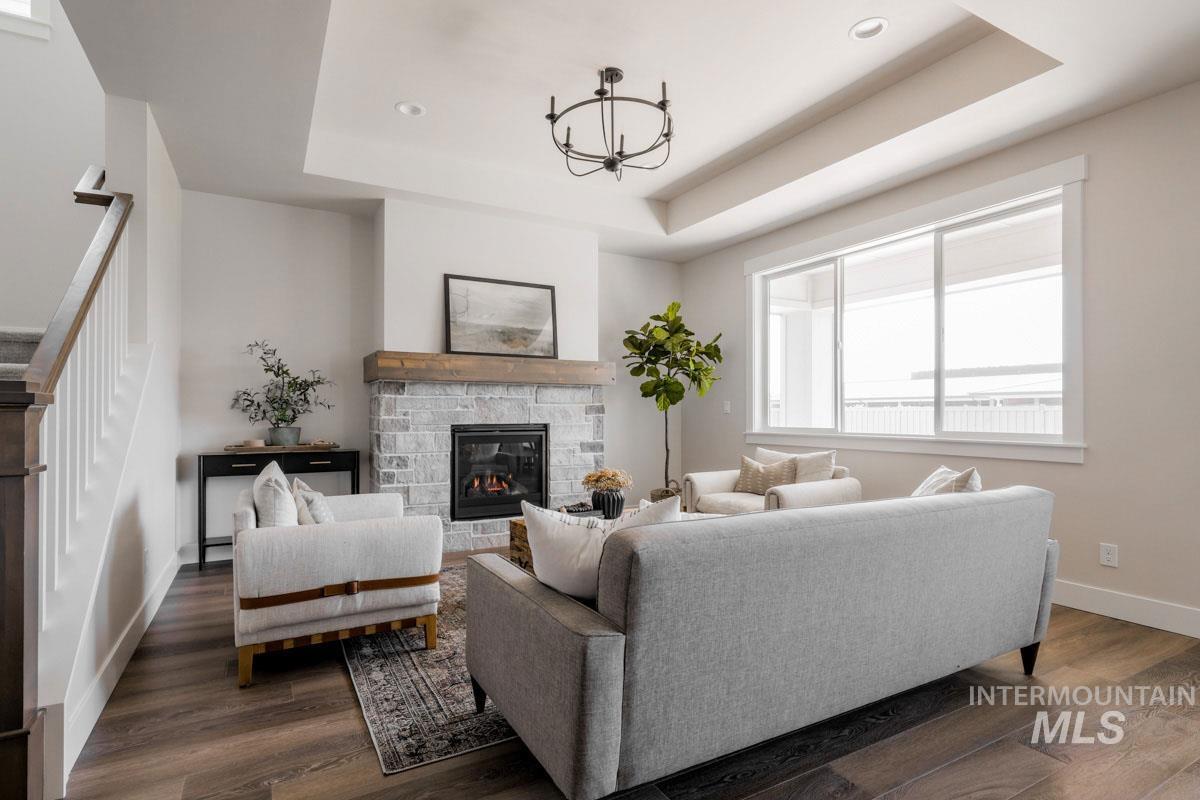 Living area with a stone fireplace, a tray ceiling, a chandelier, dark wood-type flooring, and recessed lighting