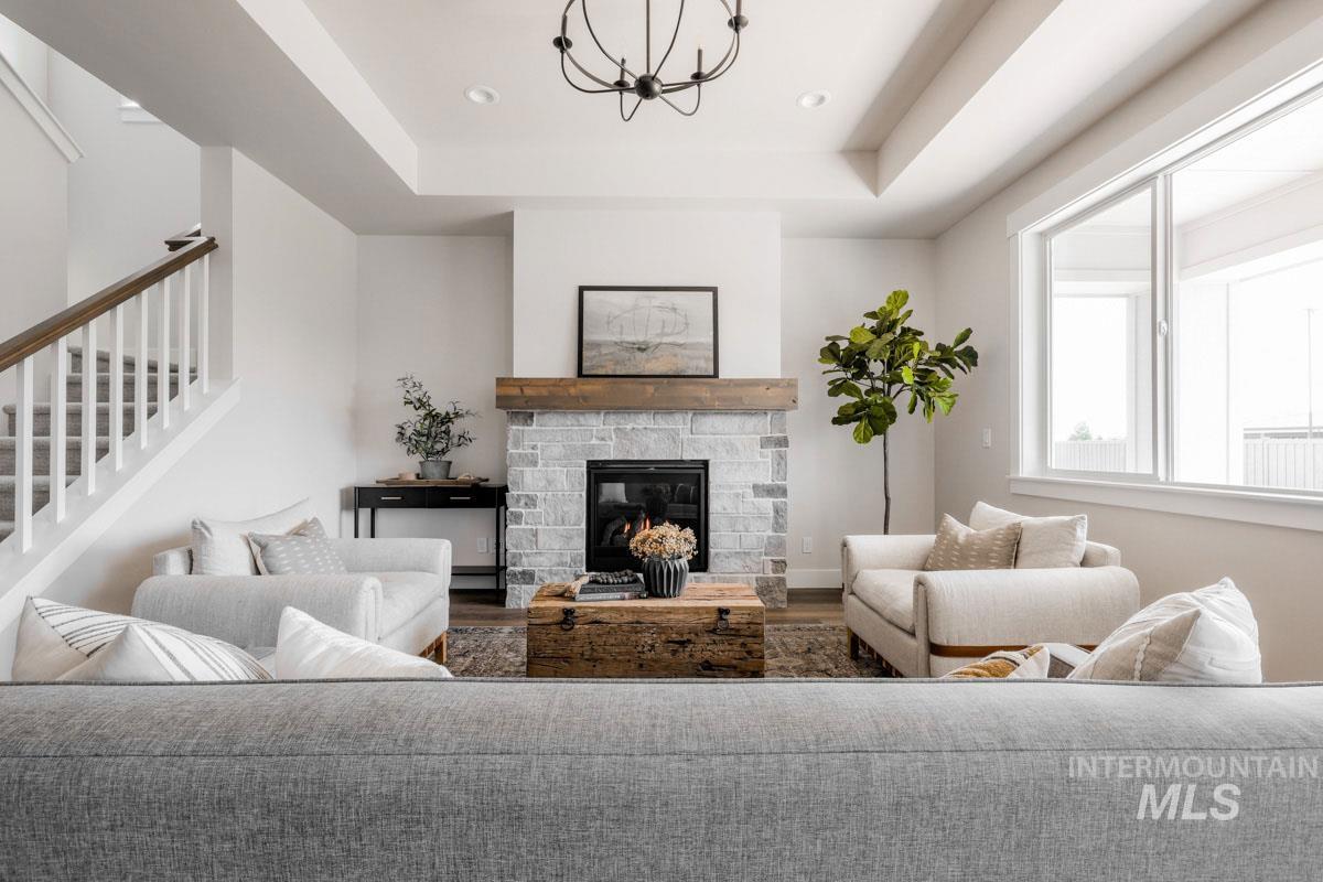 Living area with a chandelier, stairs, wood finished floors, a tray ceiling, and a fireplace