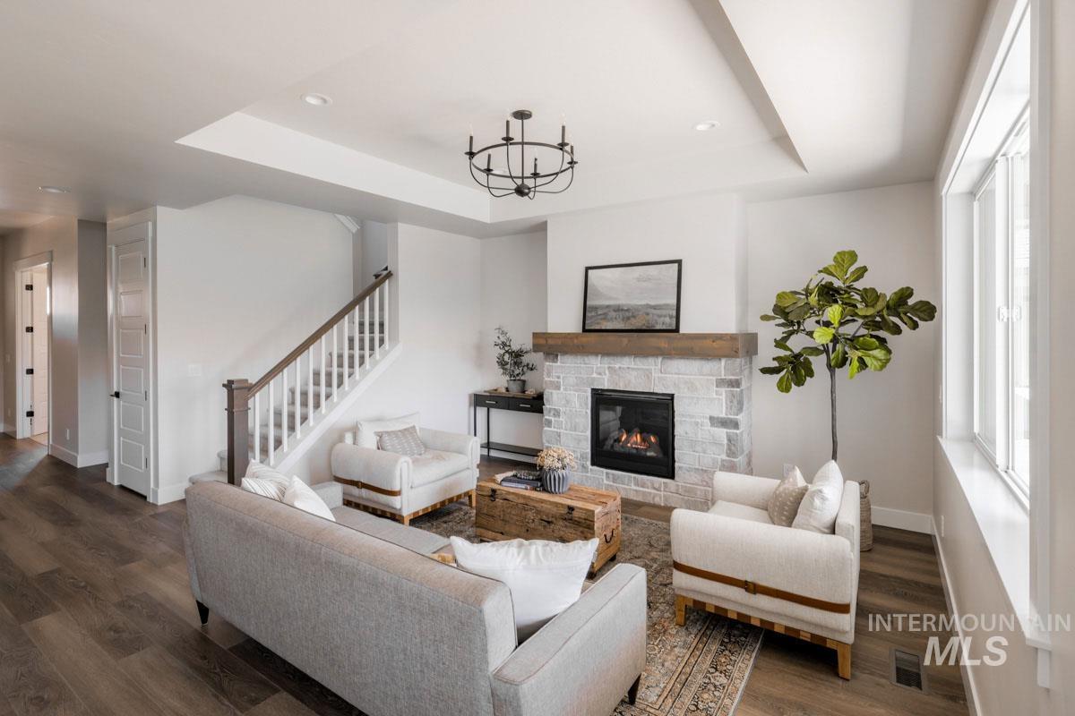 Living room featuring a chandelier, wood finished floors, a stone fireplace, a raised ceiling, and stairway