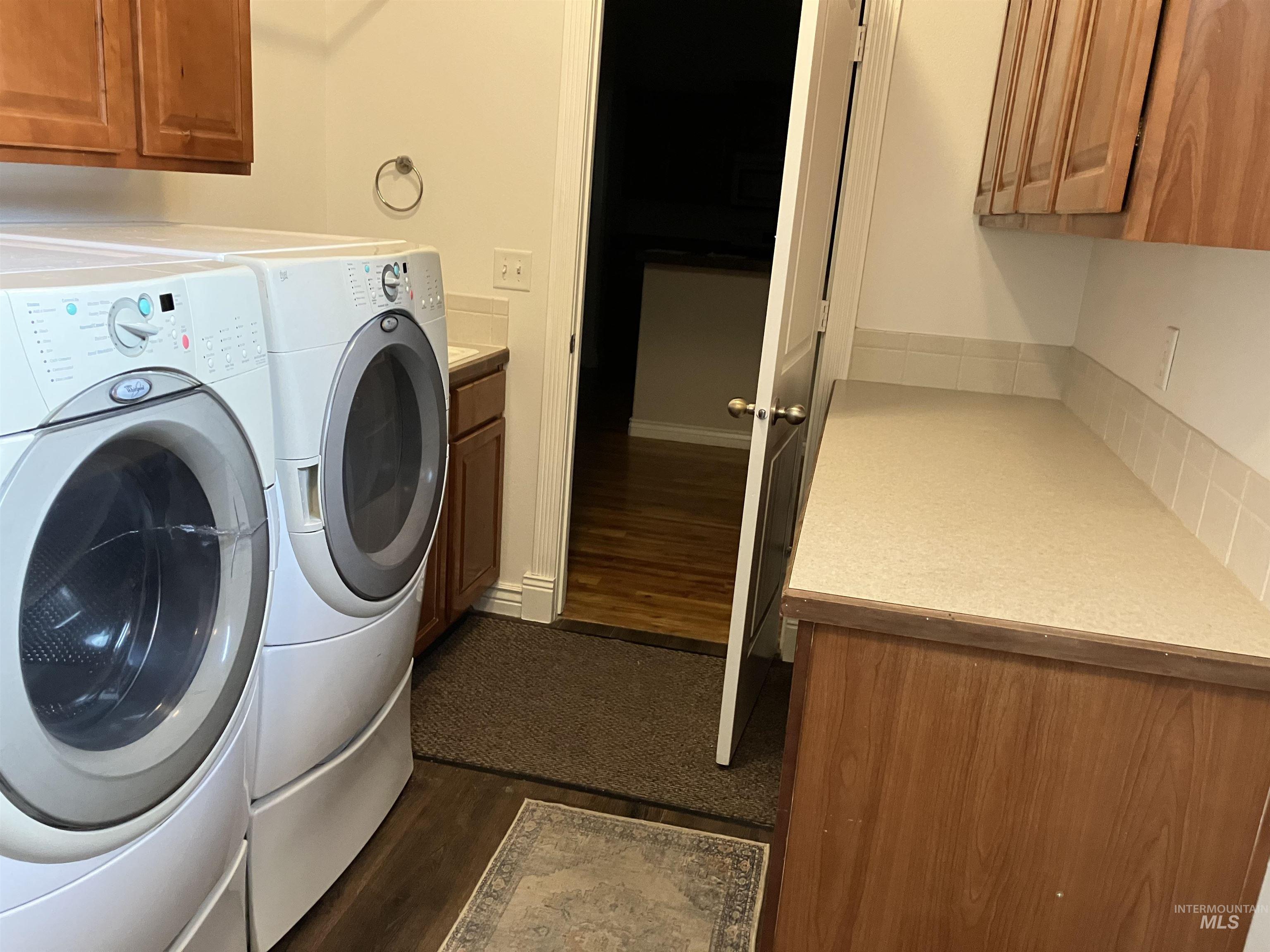 Washroom featuring dark wood-type flooring, washer and dryer, and cabinet space