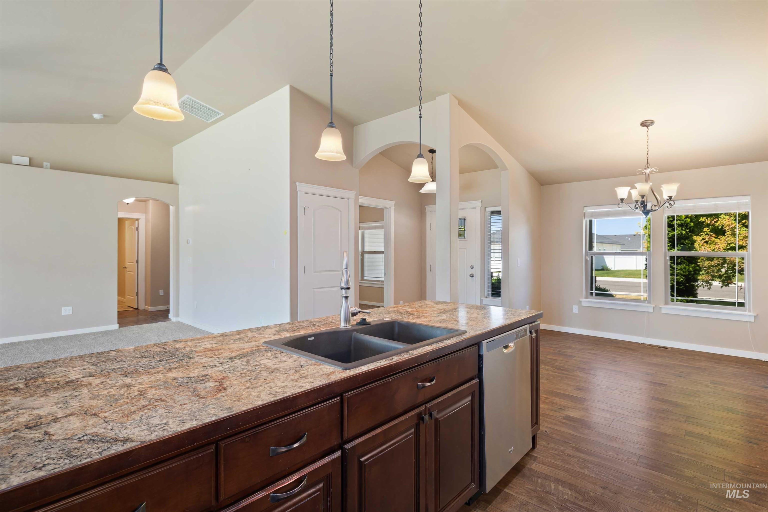 Kitchen featuring arched walkways, vaulted ceiling, dishwasher, dark brown cabinets, and a chandelier