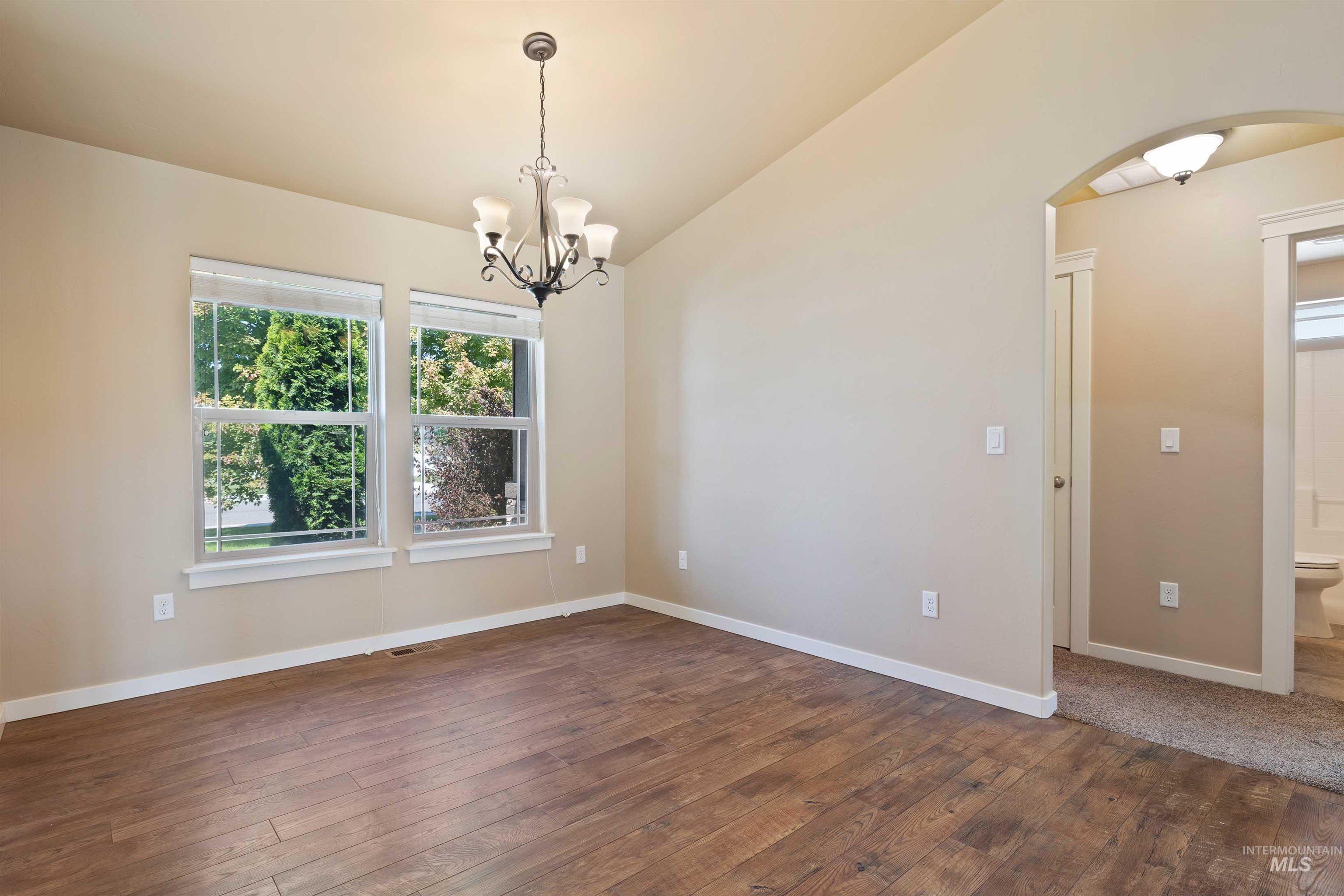 Unfurnished room with arched walkways, dark wood-style floors, lofted ceiling, and a chandelier