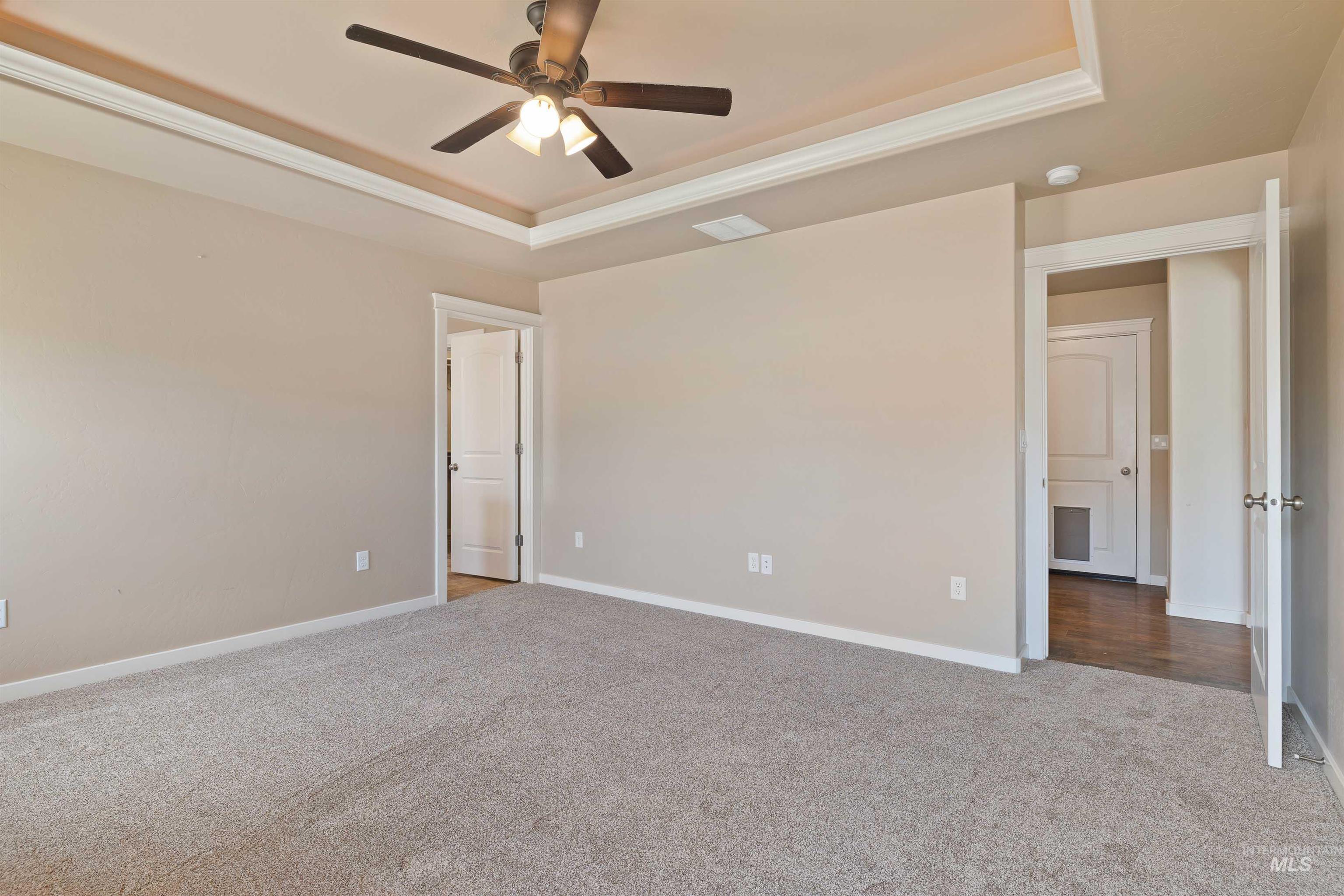 Unfurnished bedroom with a tray ceiling, carpet floors, crown molding, and a ceiling fan