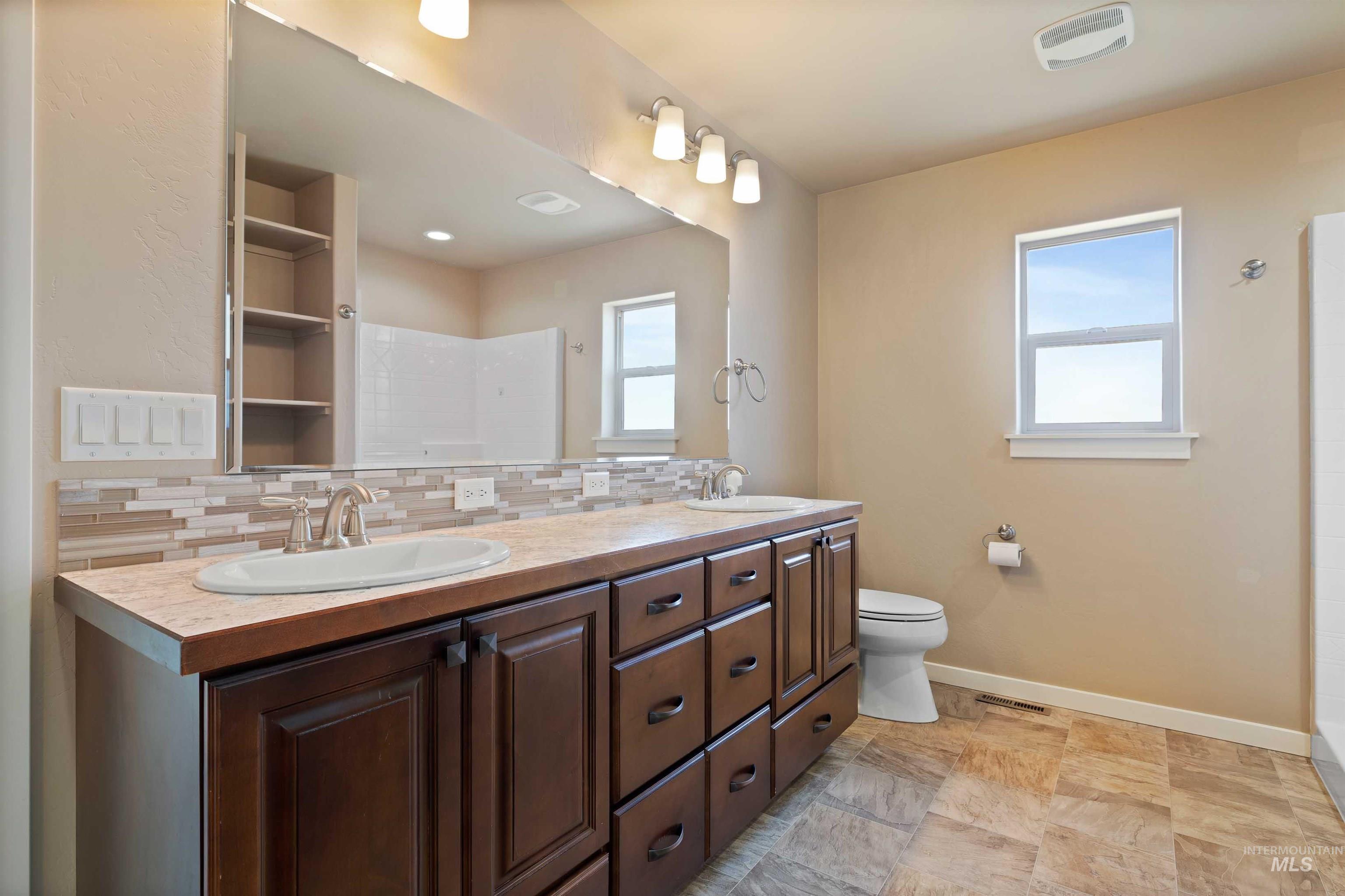 Bathroom with double vanity, a tile shower, and tasteful backsplash