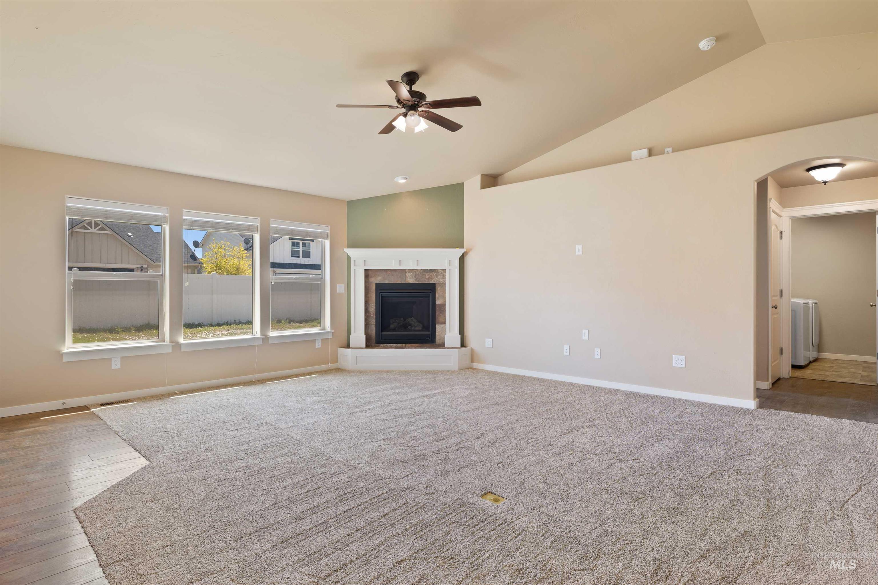 Unfurnished living room with arched walkways, lofted ceiling, ceiling fan, a tiled fireplace, and wood-type flooring