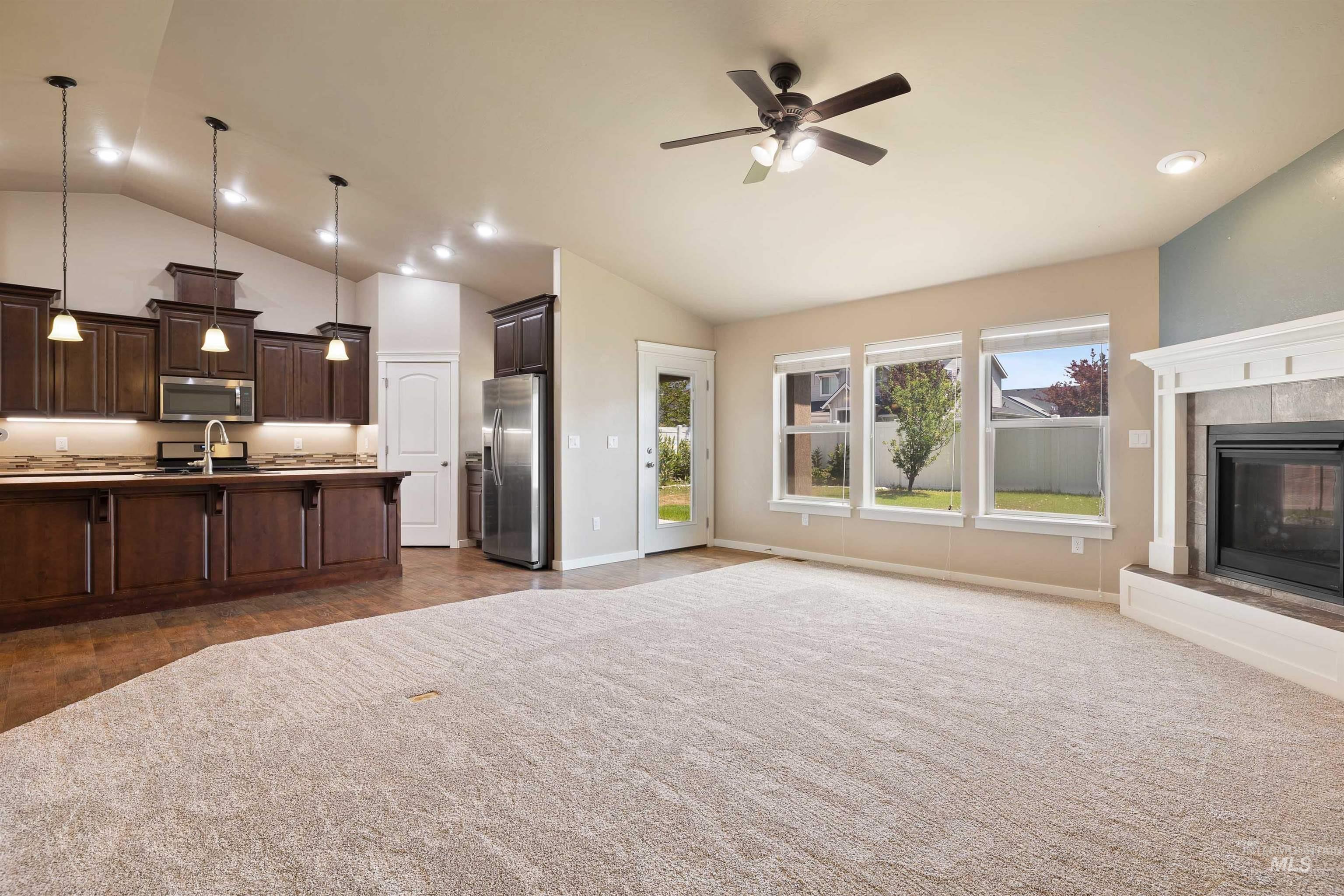 Kitchen with stainless steel appliances, open floor plan, dark brown cabinets, a ceiling fan, and hanging light fixtures