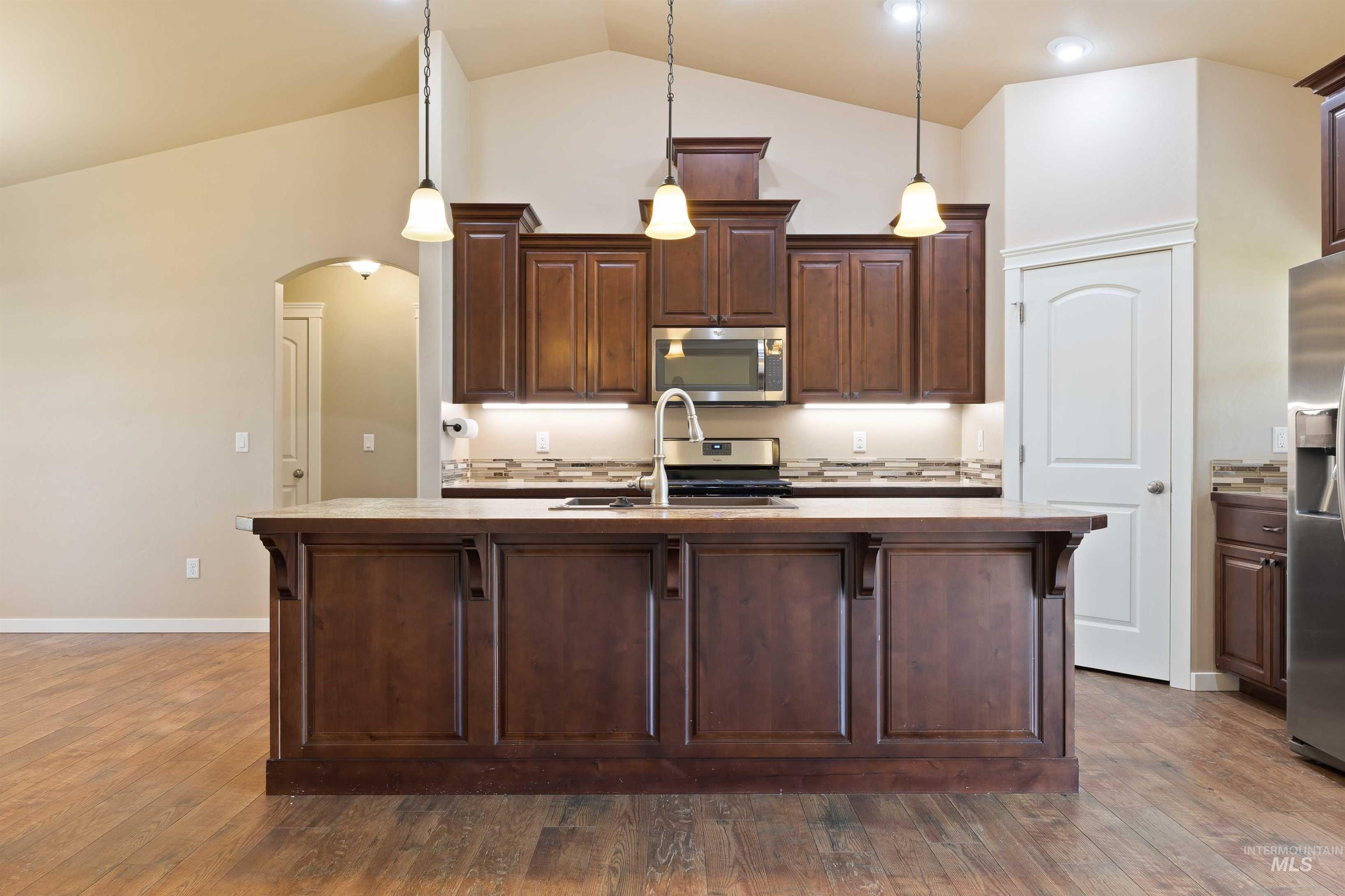 Kitchen with appliances with stainless steel finishes, vaulted ceiling, arched walkways, dark brown cabinetry, and dark wood-type flooring