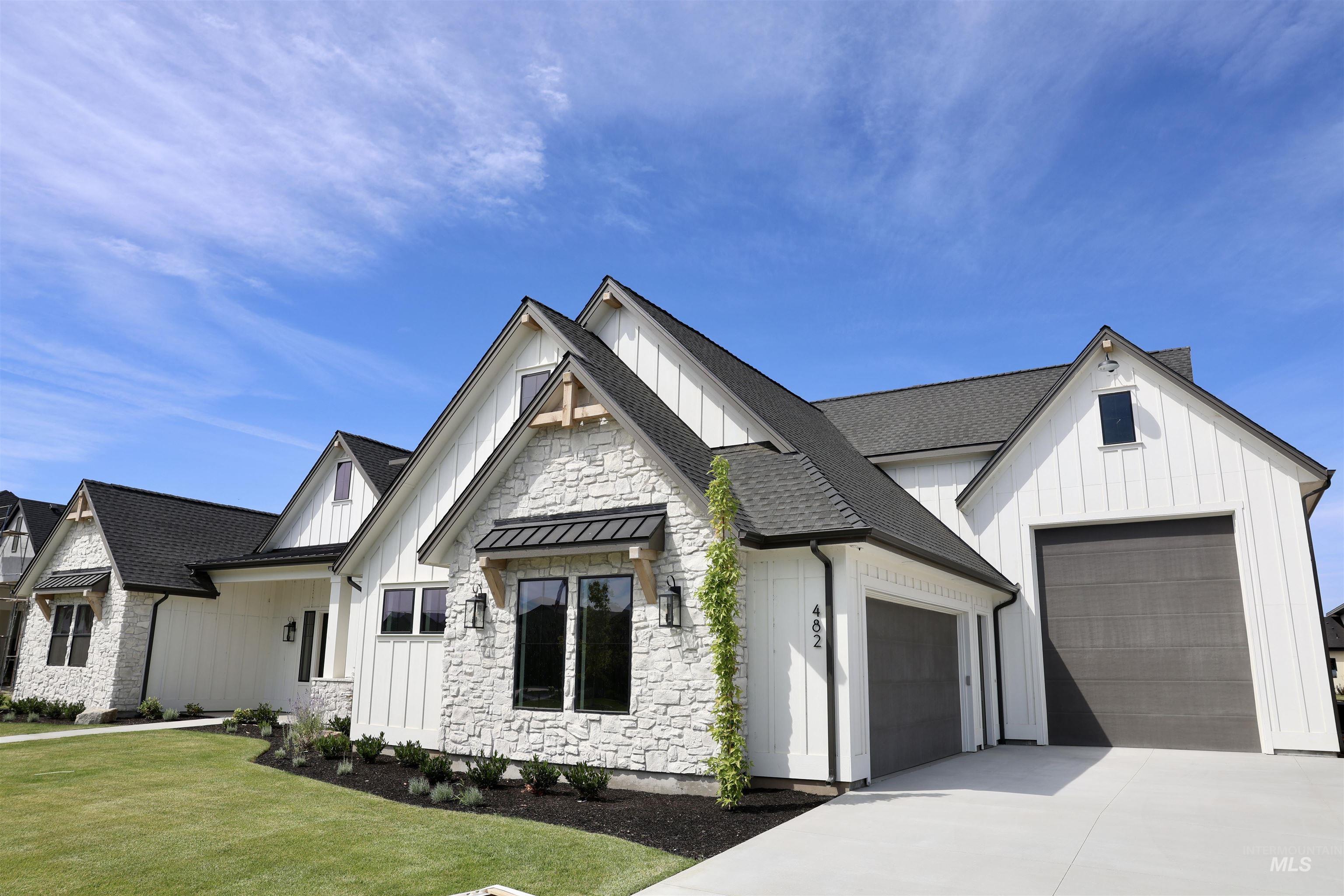 Modern farmhouse with board and batten siding, roof with shingles, driveway, and stone siding