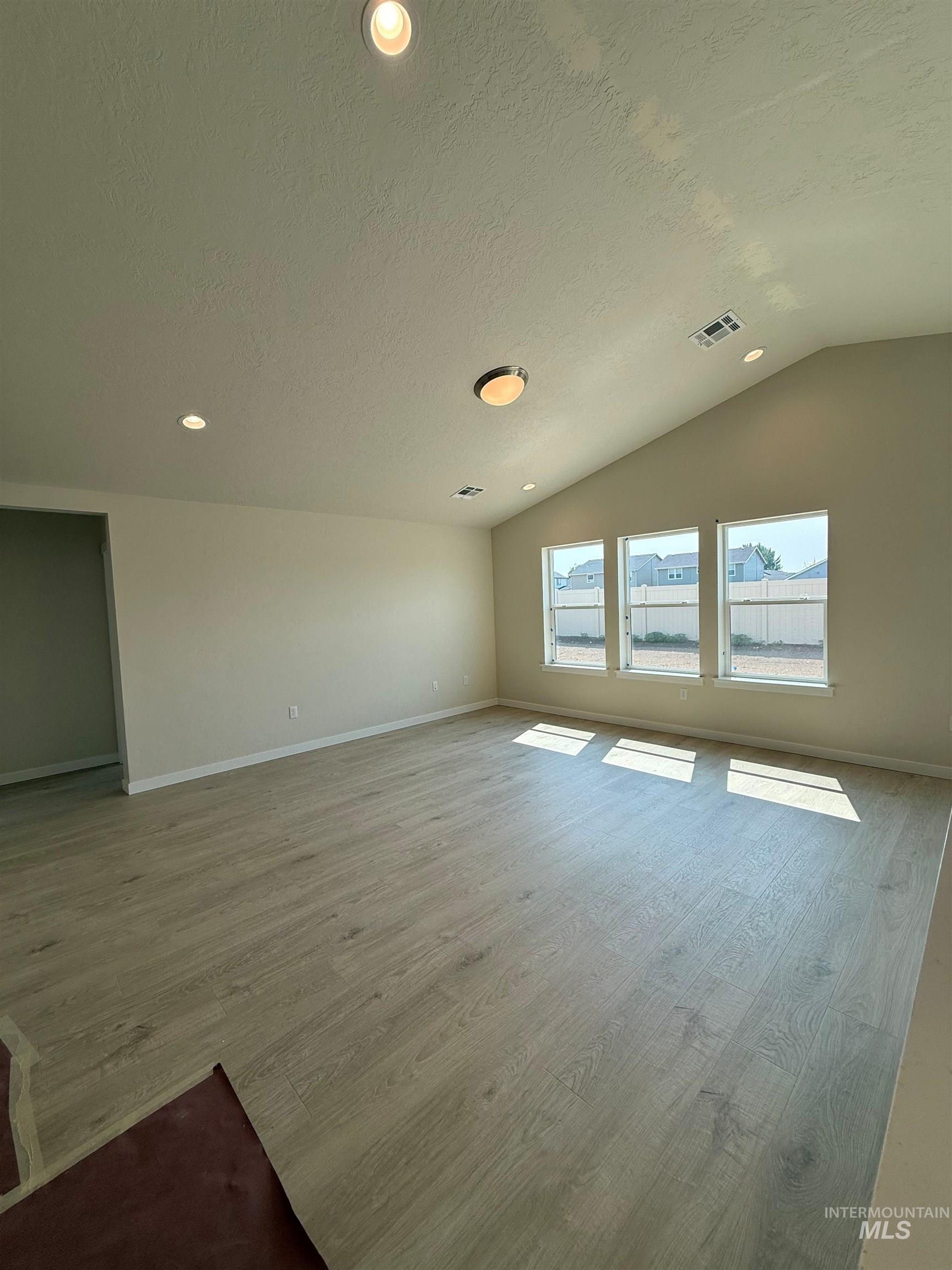 Unfurnished living room featuring lofted ceiling, light wood-style floors, recessed lighting, and a textured ceiling