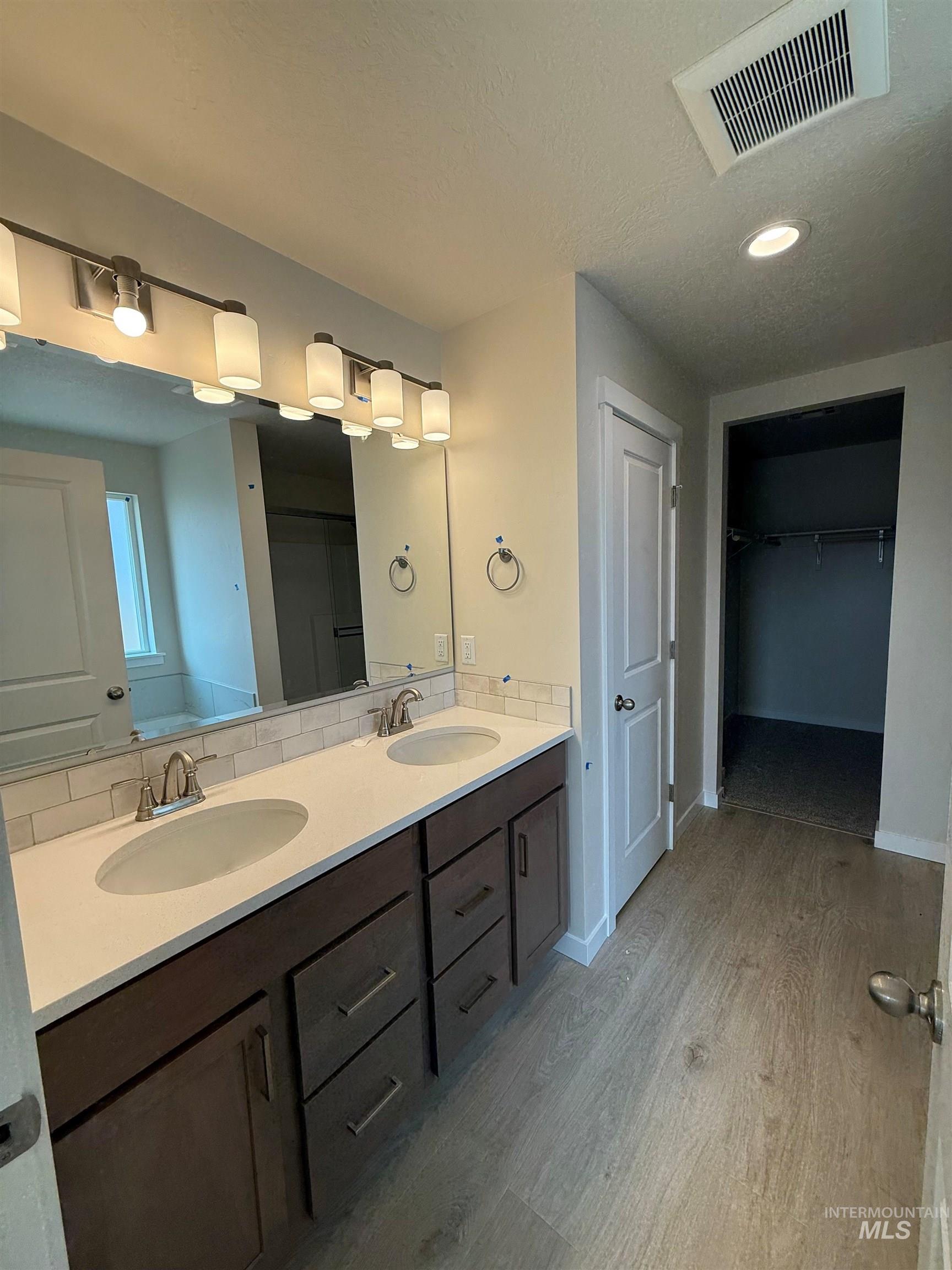 Full bathroom with double vanity, a walk in closet, light wood-style flooring, recessed lighting, and a textured ceiling