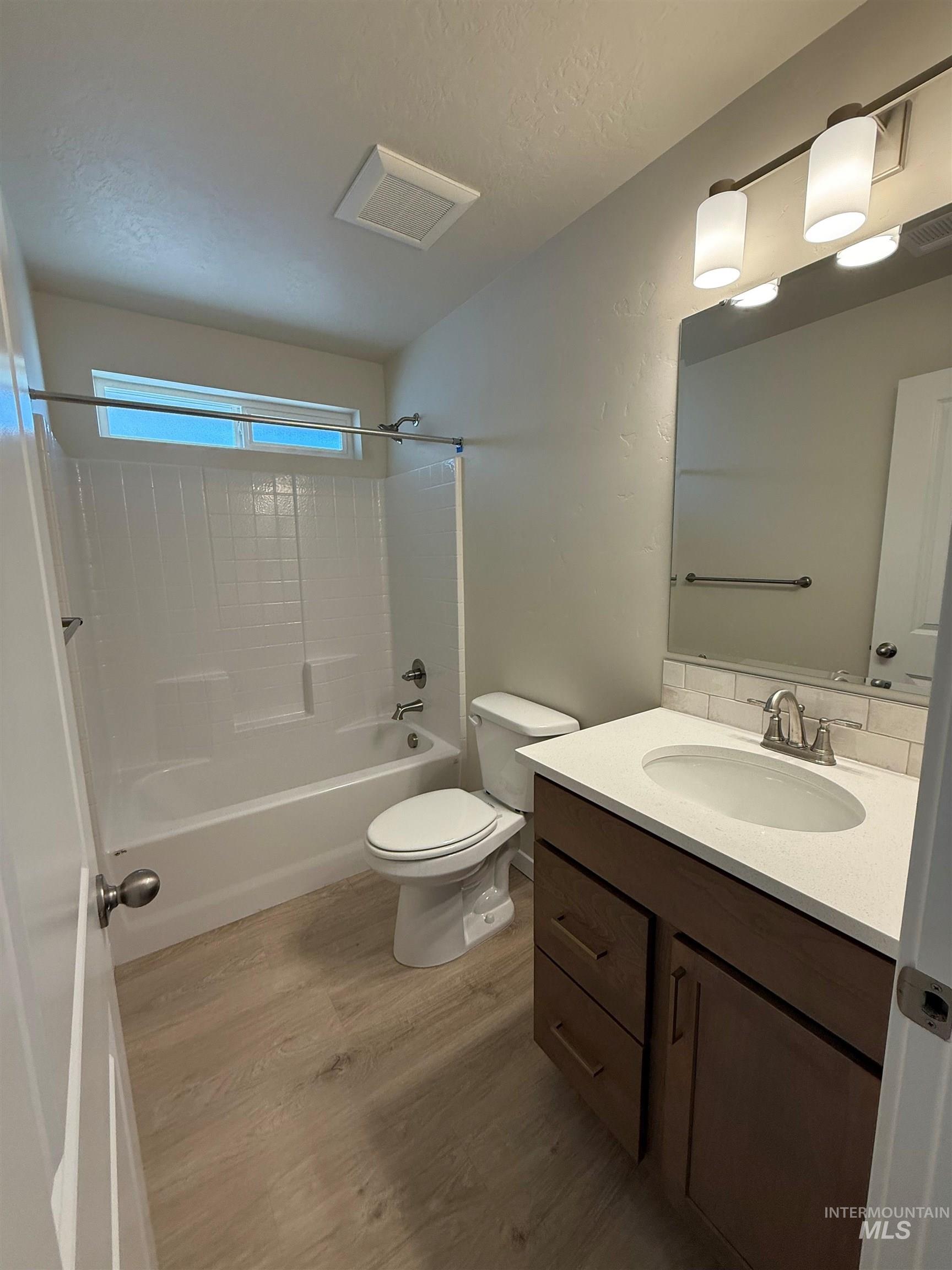 Full bath with bathing tub / shower combination, vanity, light wood-style floors, and a textured ceiling
