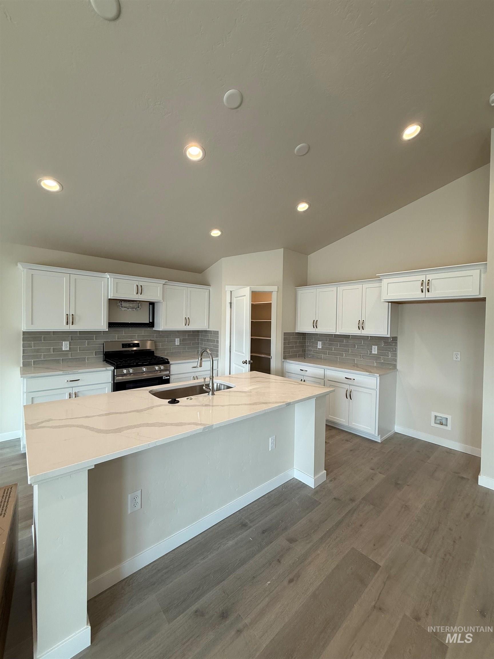 Kitchen featuring backsplash, white cabinetry, light stone counters, recessed lighting, and a center island with sink