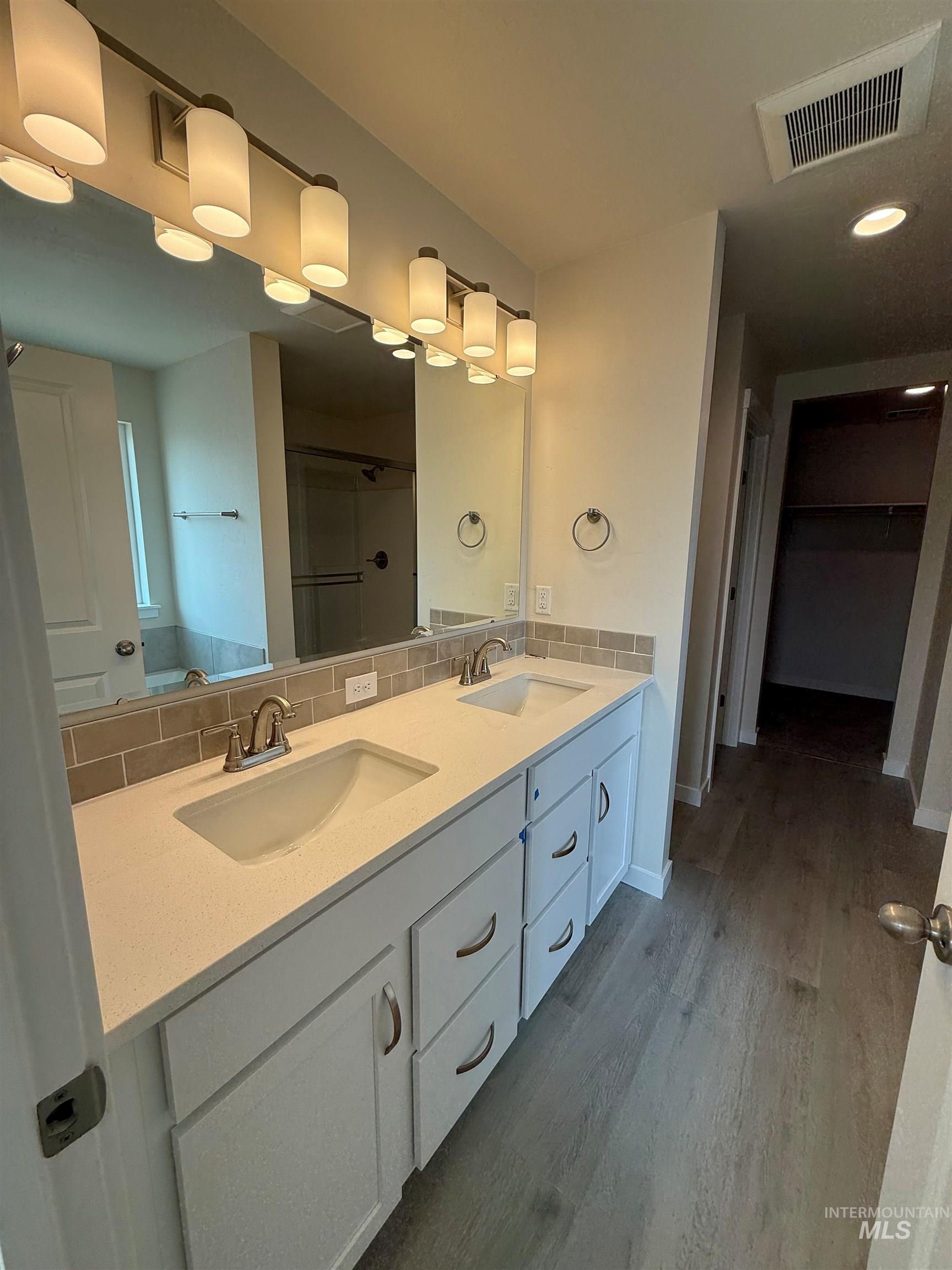 Full bath featuring wood finished floors, a stall shower, double vanity, backsplash, and a walk in closet
