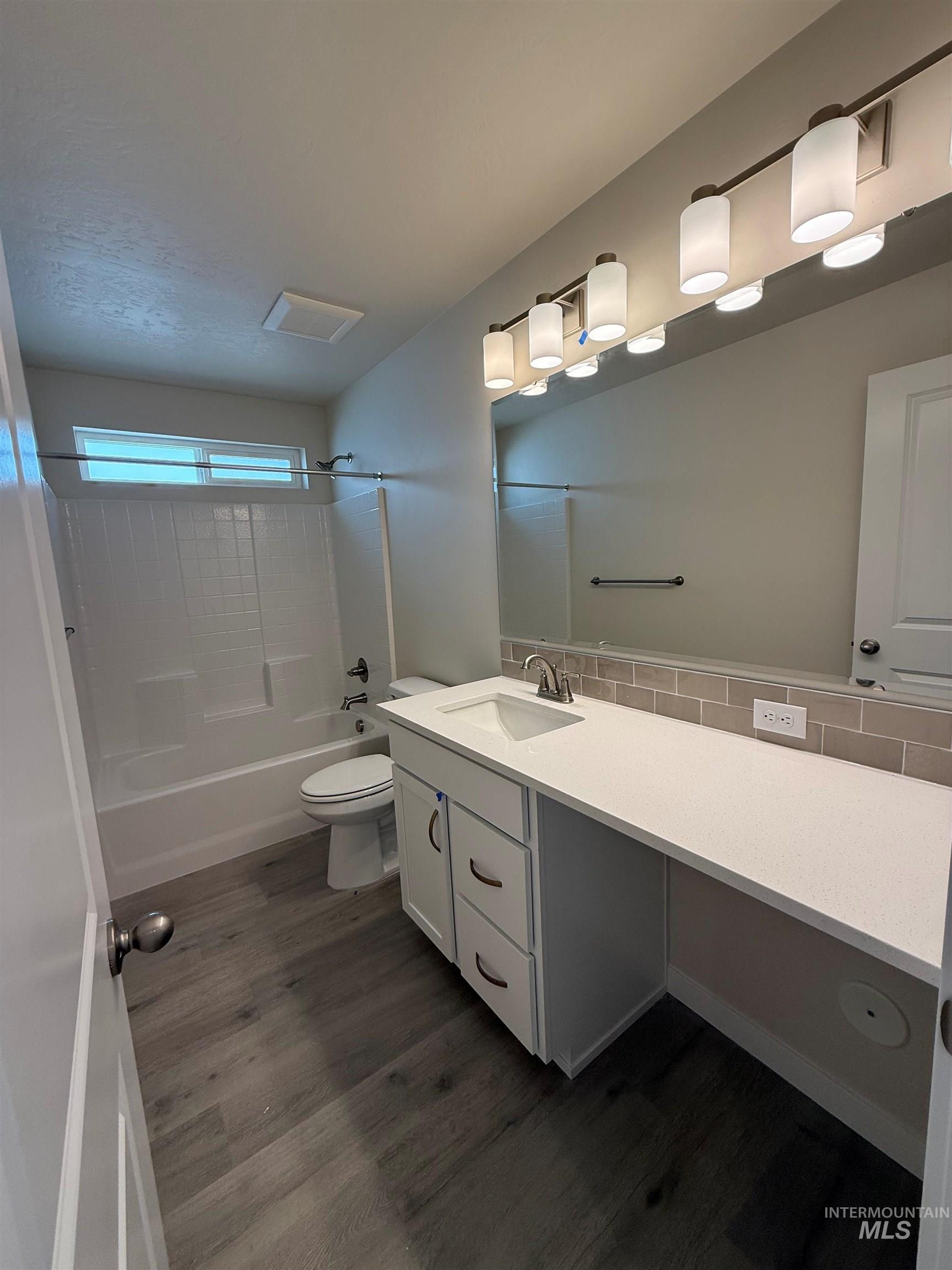 Full bath with shower / bath combination, dark wood finished floors, vanity, and backsplash
