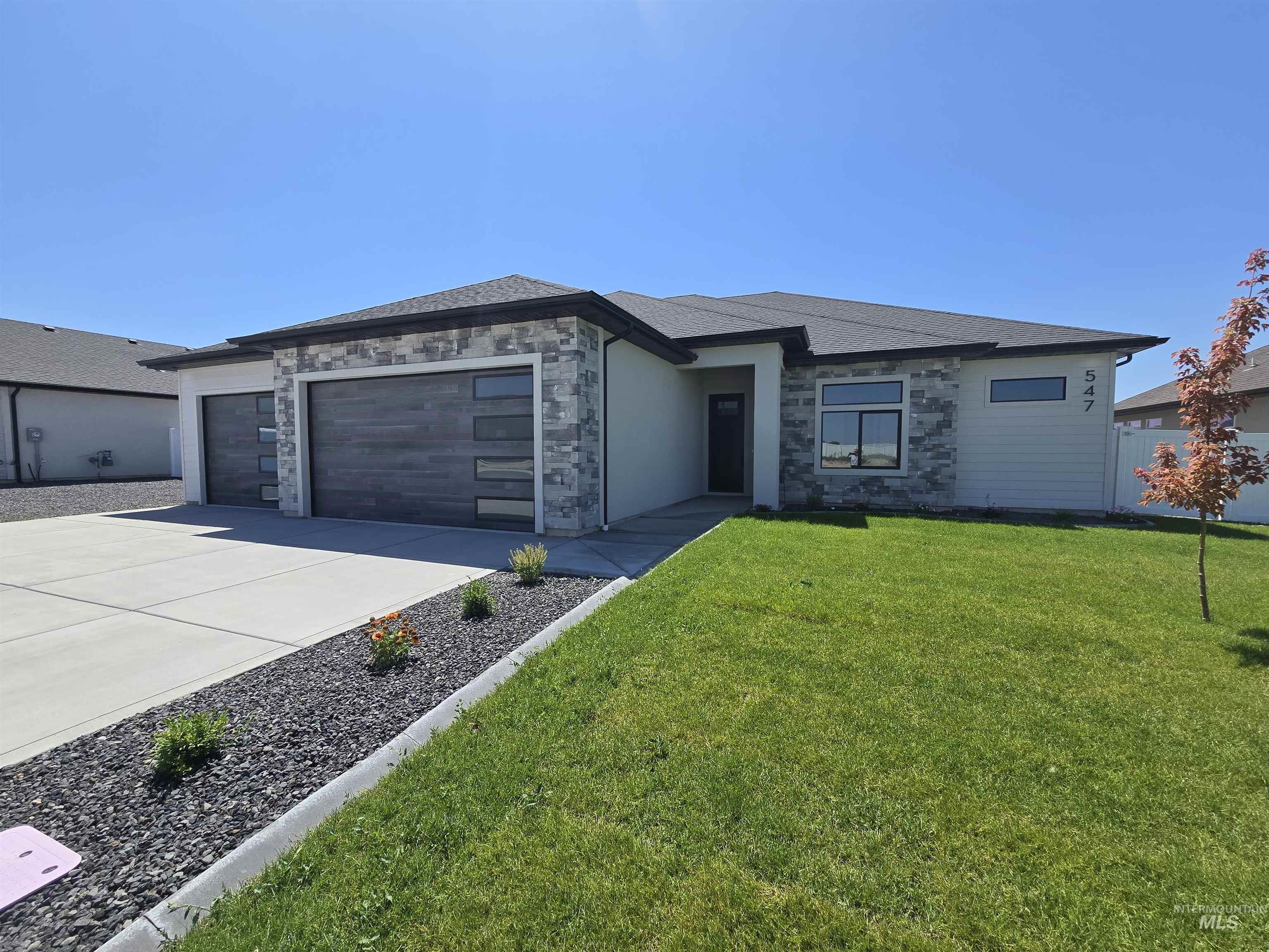 Prairie-style home with a garage, stone siding, concrete driveway, and a front yard