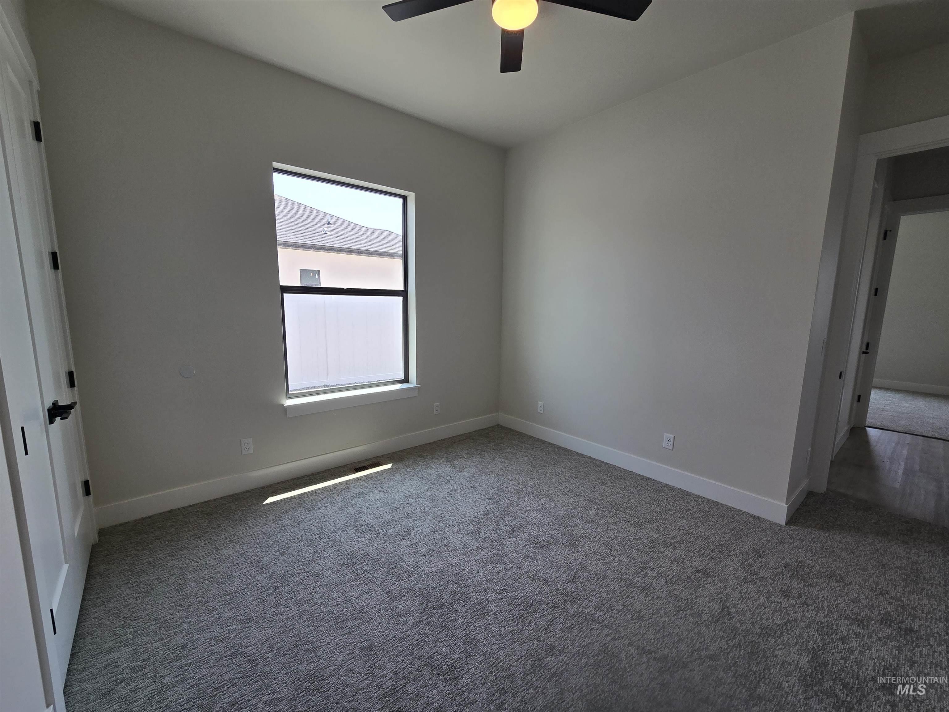 Carpeted spare room with ceiling fan and baseboards
