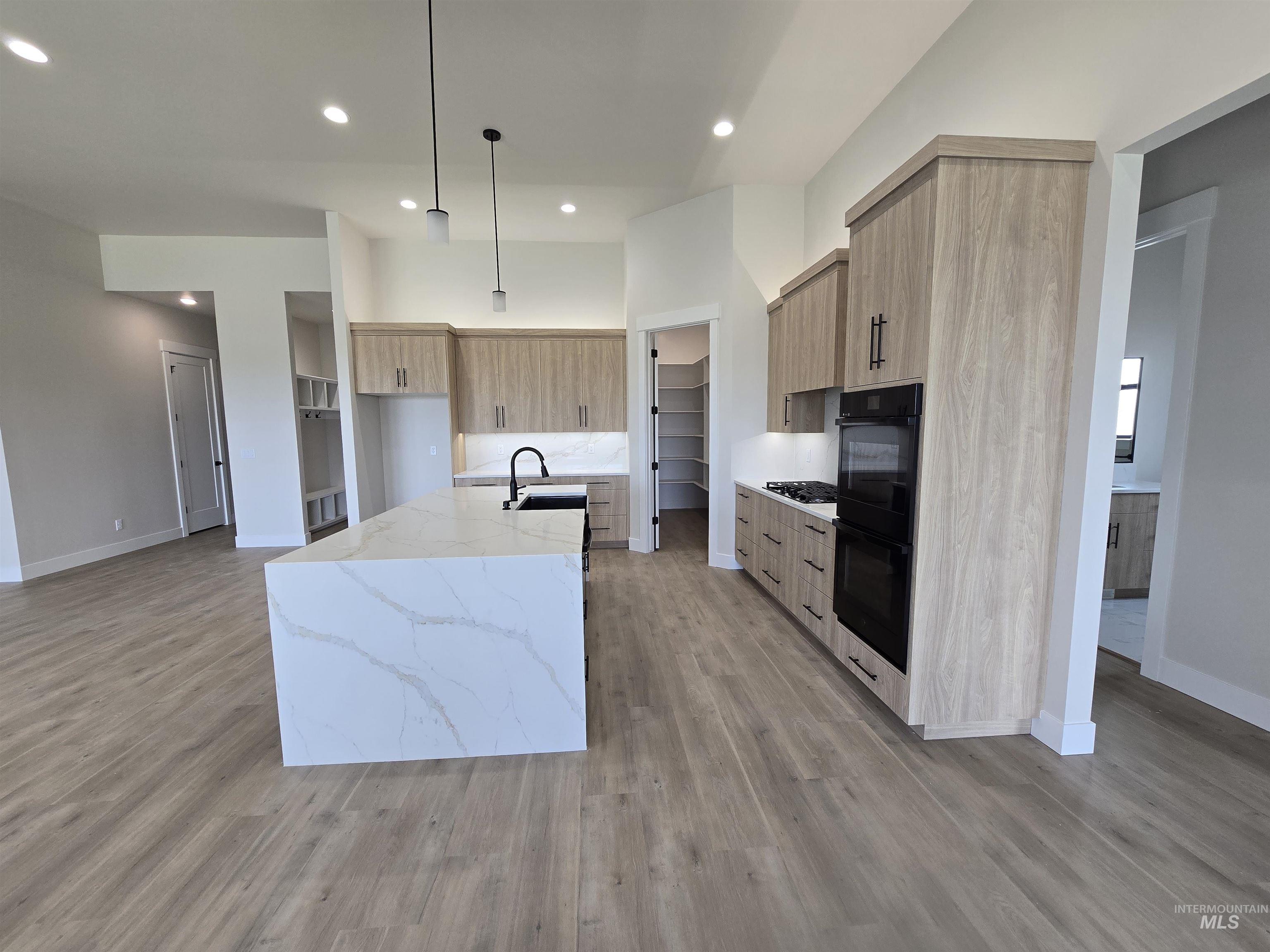 Kitchen featuring modern cabinets, an island with sink, light wood-style flooring, light stone counters, and gas stovetop