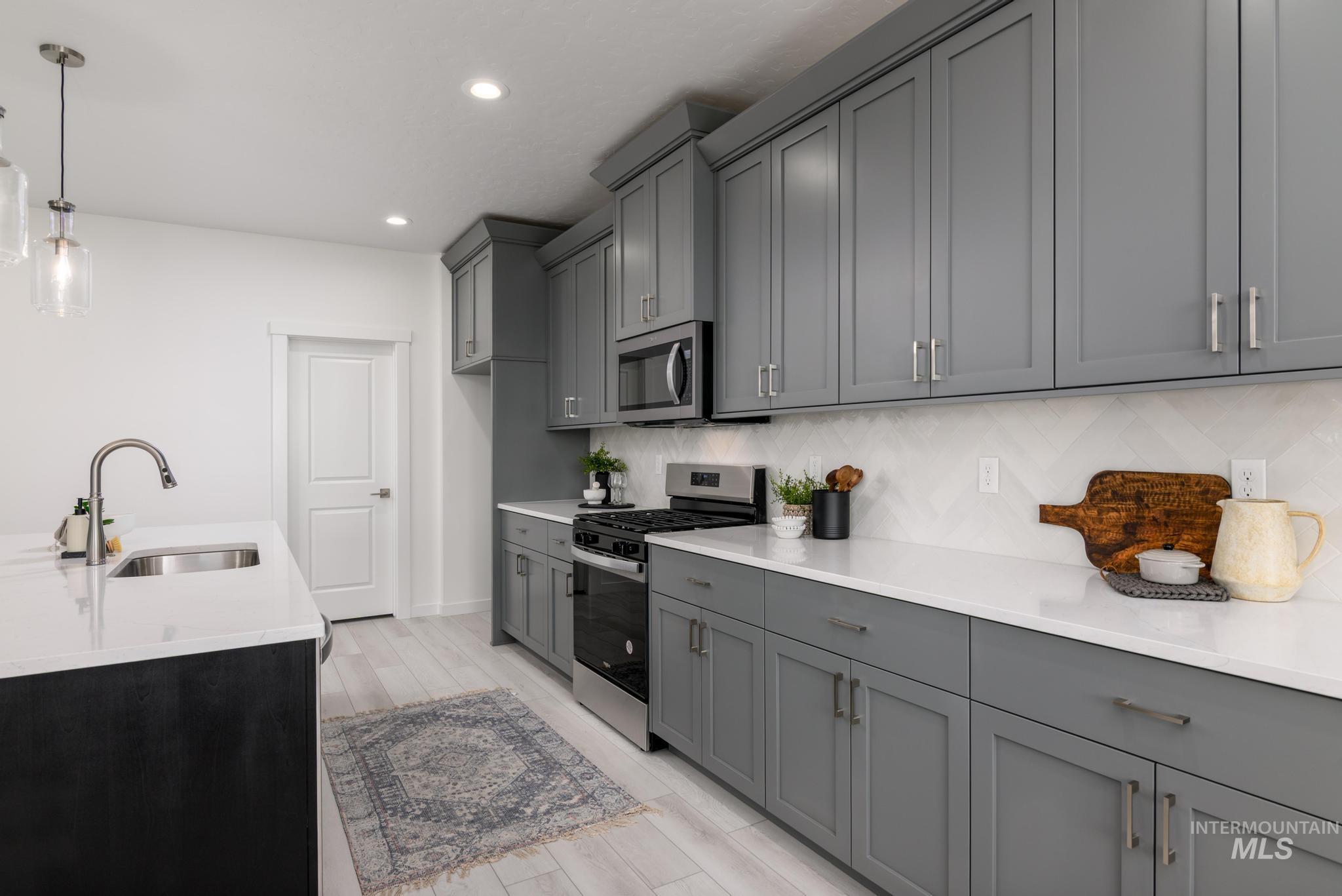 Kitchen featuring stainless steel appliances, gray cabinets, decorative backsplash, recessed lighting, and light countertops
